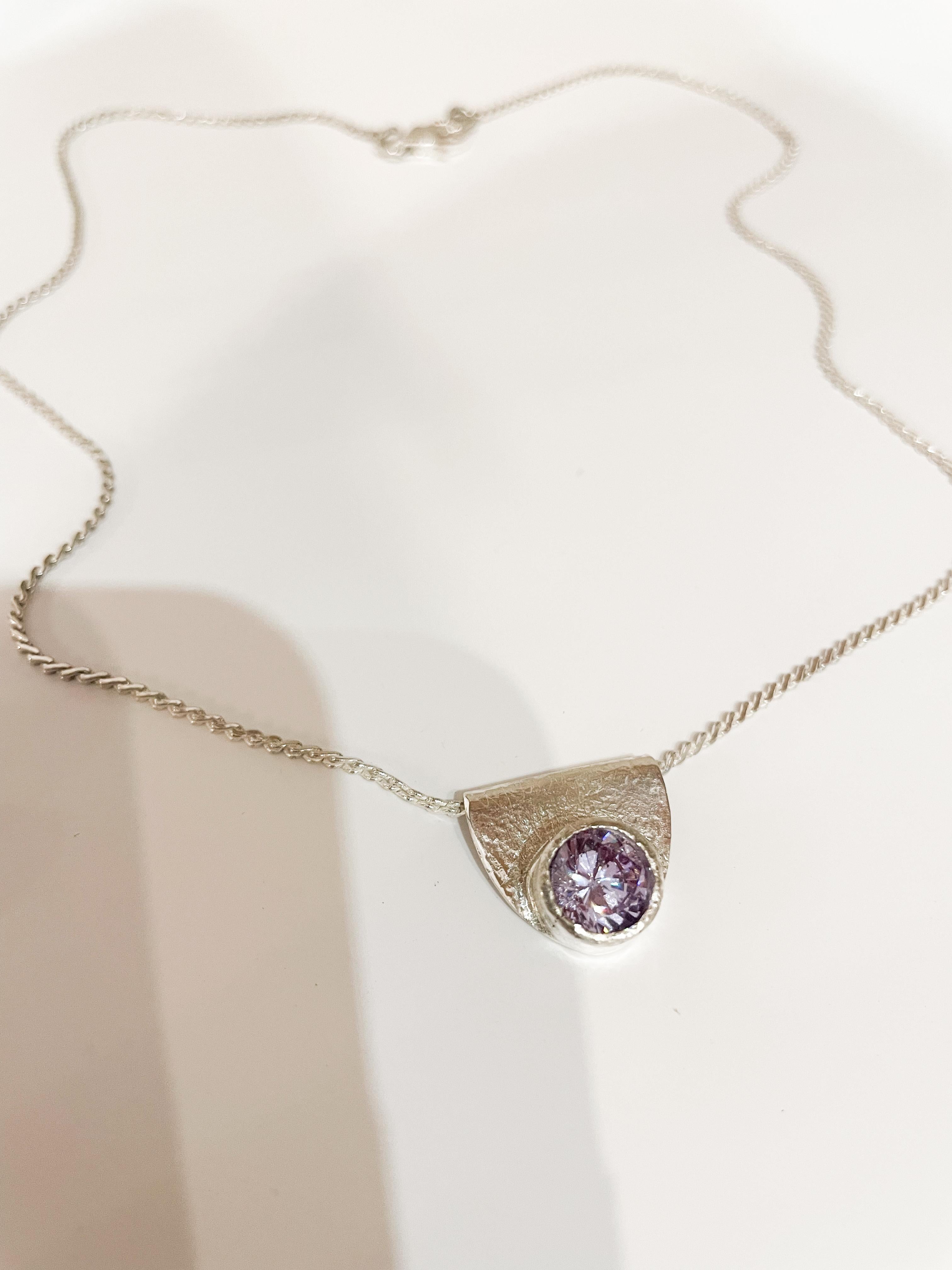 Este collar artesanal, creado en plata de ley 925 maciza, lleva un delicado colgante adornado con una brillante piedra de circonita lila. Diseñado pensando en la sencillez y la sofisticación, el Collar Suave añade un toque refinado a cualquier look,