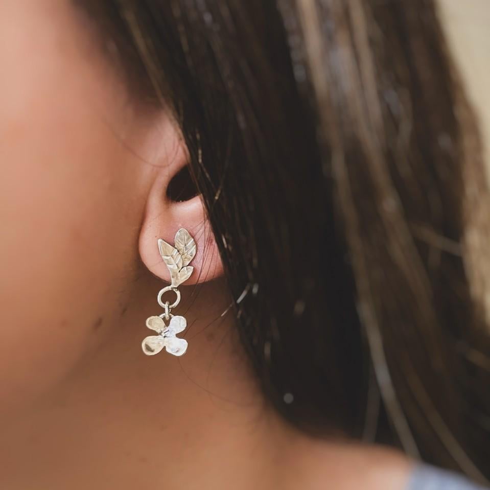 These elegant earrings are handcrafted in solid 925 sterling silver, combining the charm of small dangling leaves with delicate mini flowers. Inspired by nature, their subtle movement and organic shapes create a piece that is both graceful and