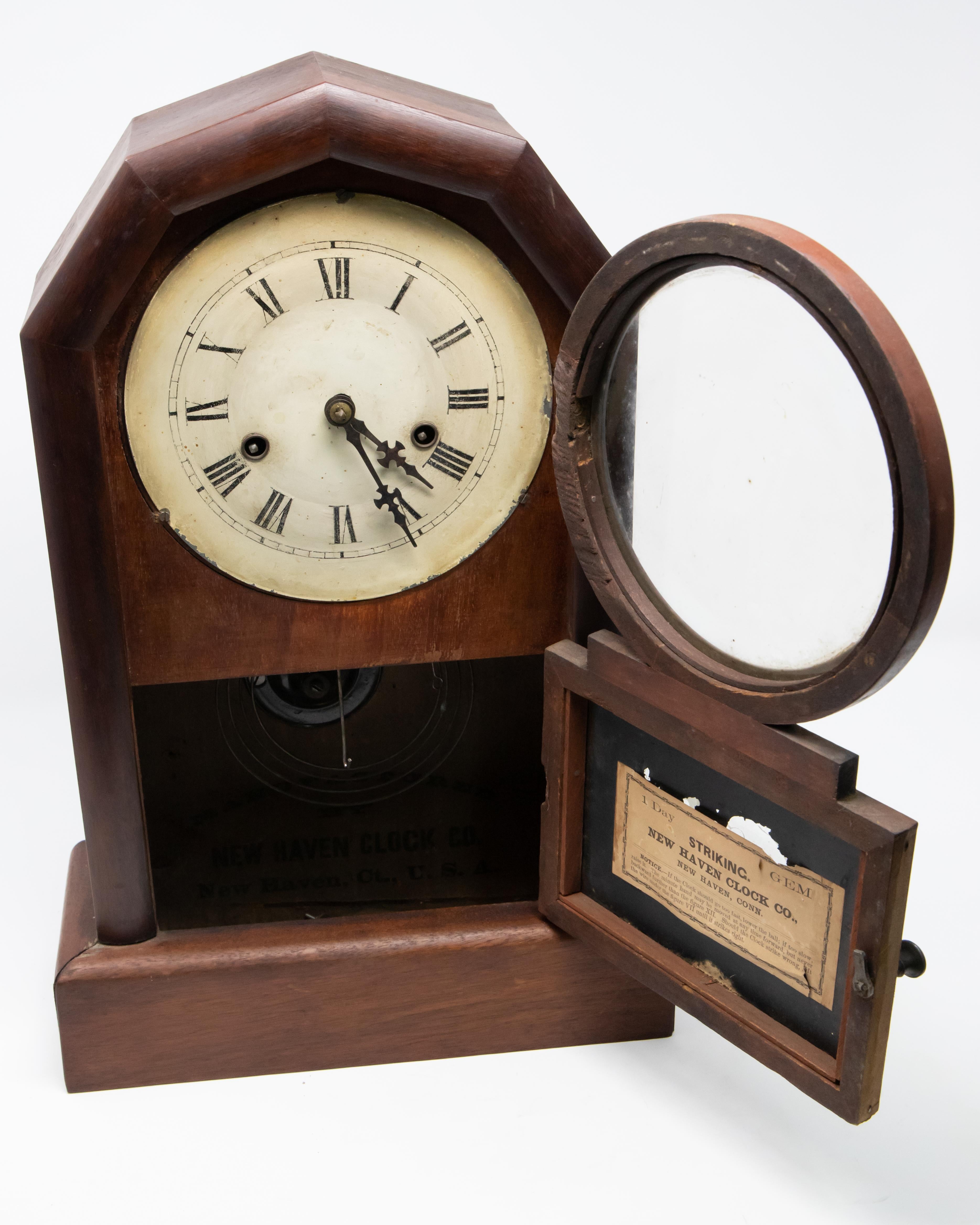 Mantle clock by New Haven Clock Co. Simple lines make this clock so easy to see. Starting on a rectangular base it rises very squarely. At the top there are angles to make an arch. The face of the clock is enamel with roman numerals. Reverse