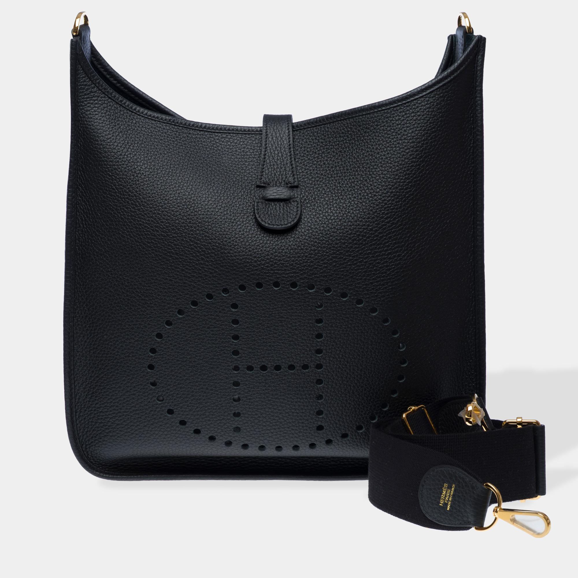 Iconic​ ​Hermès​ ​Evelyne​ ​GM​ ​shoulder​ ​bag​ ​in​ ​black​ ​Taurillon​ ​Clemence​ ​leather,​ ​gold​ ​metal​ ​trim,​ ​removable​ ​black​ ​canvas​ ​shoulder​ ​strap​ ​allowing​ ​for​ ​shoulder​ ​or​ ​crossbody​ ​carry

Snap​ ​button​ ​closure​ ​on​