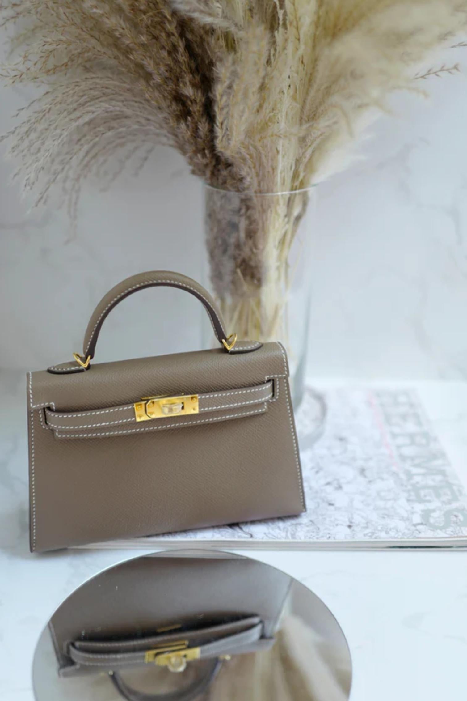 Le Mini Kelly d'Hermès en cuir d'Etoupe Epsom et quincaillerie dorée est une parfaite harmonie entre sophistication et charme. Fabriquée à la main en France, cette pièce convoitée met en valeur le savoir-faire artisanal de la maison, des coutures