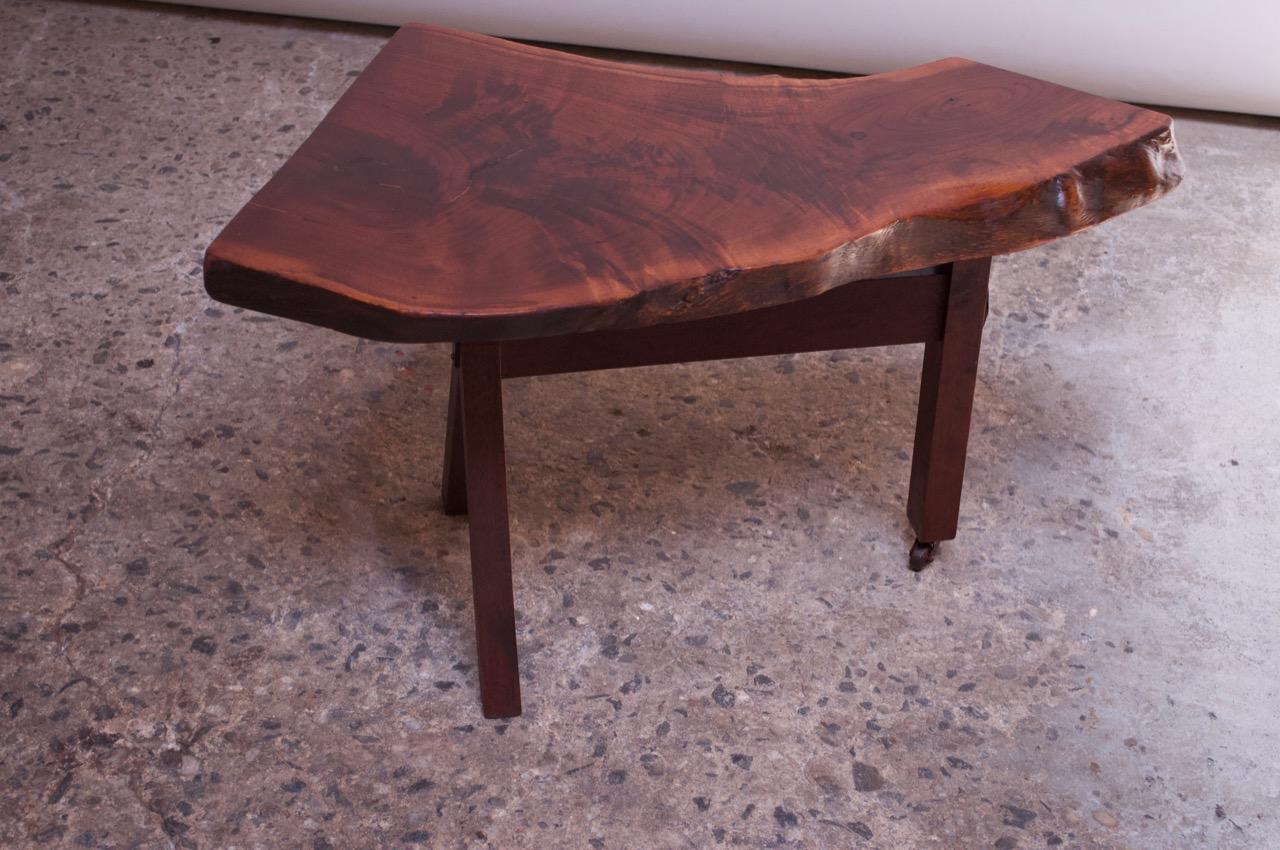 Expertly crafted circa 1950s walnut live edge side / occasional table with three-legged base. Additional details include 2 carved plates mounted on both the front and back legs for decoration. One of the legs features a caster wheel to allow for