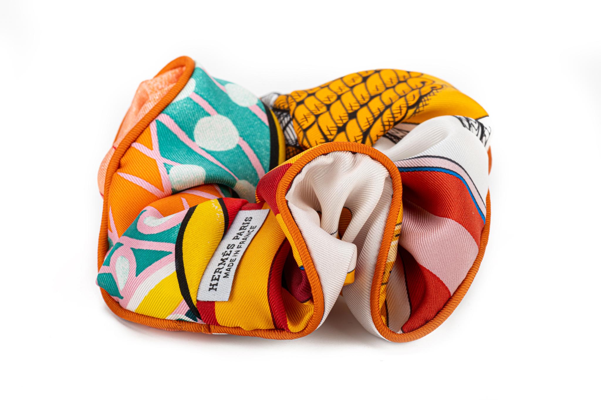 Hermes brand new in box orange silk scrunchie. The pattern can vary from one item to another. Being cut from a multicolor and multi pattern scarf will result in variations of the same chouchou. The piping is the only consistent factor and can be a
