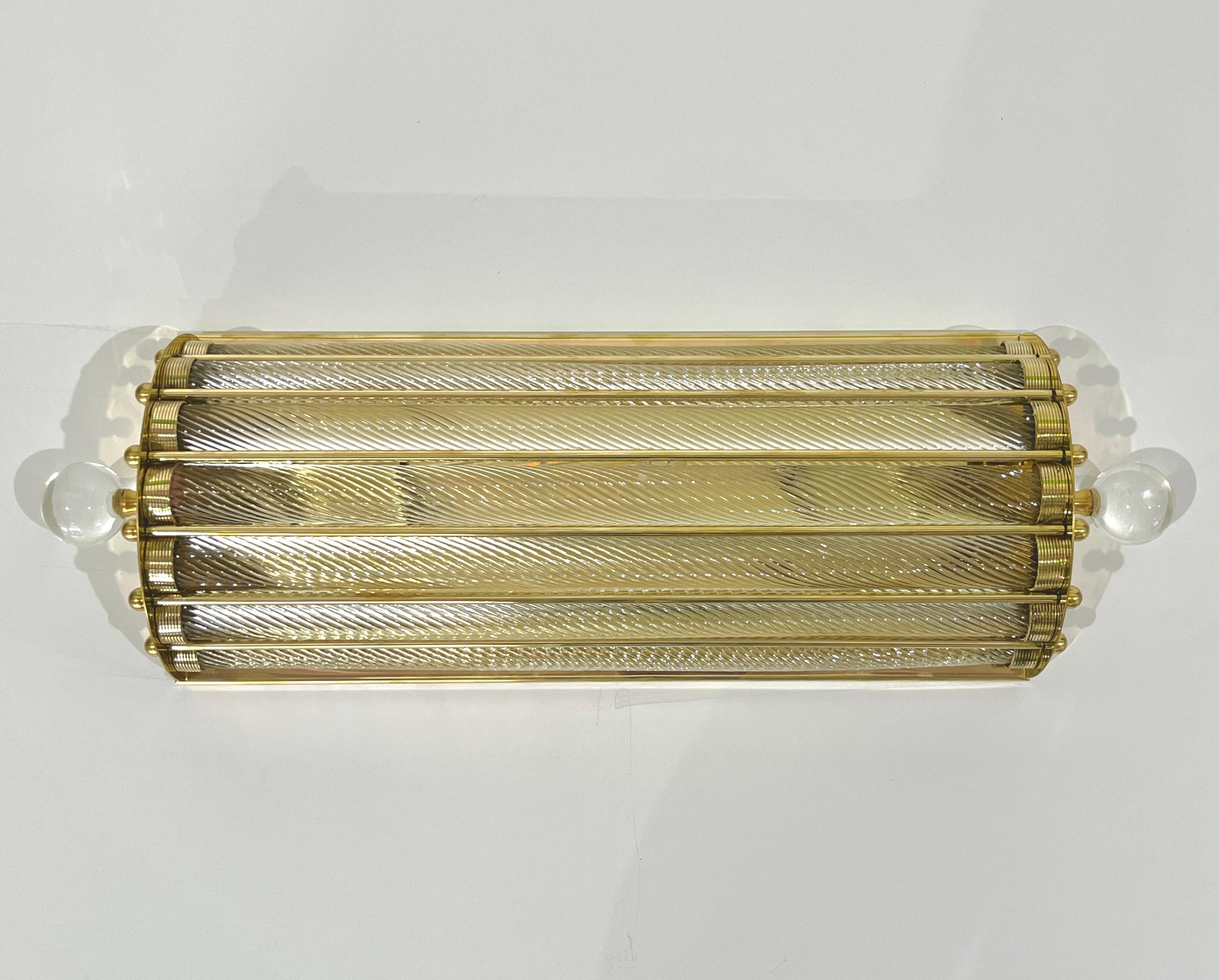 Contemporary customizable Italian Art Deco design pair of semi-circular wall lights or flush mounts, entirely handcrafted in brass. The nicely scalloped airy brass structure supports 7 crystal clear Murano glass rods worked with the sophisticated