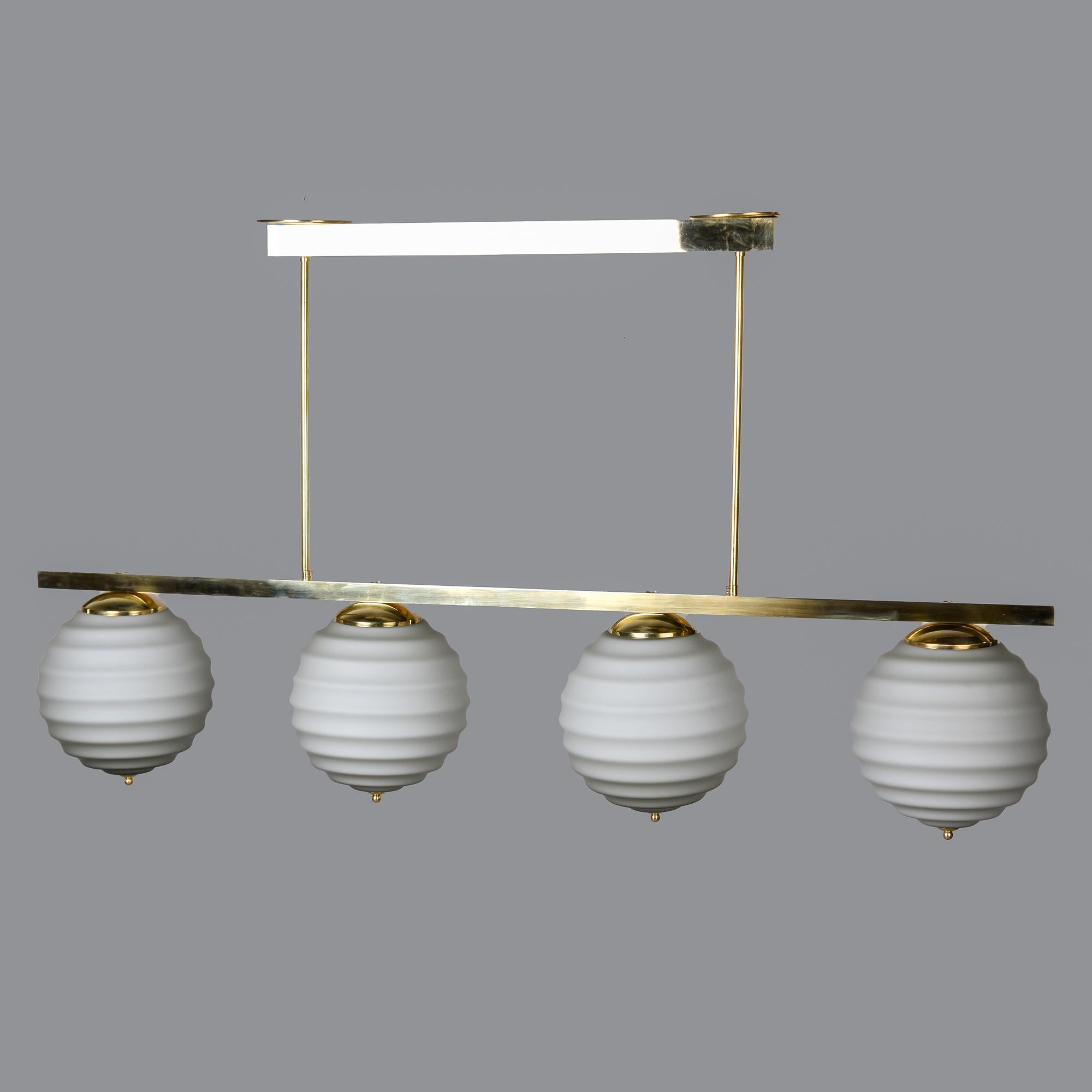 Nouveau luminaire à quatre lumières en verre et laiton importé d'Italie. Base et chapiteau en laiton poli, avec quatre globes en verre. Les globes sont de couleur taupe très pâle et ont une texture de surface striée. L'appareil a été câblé selon les