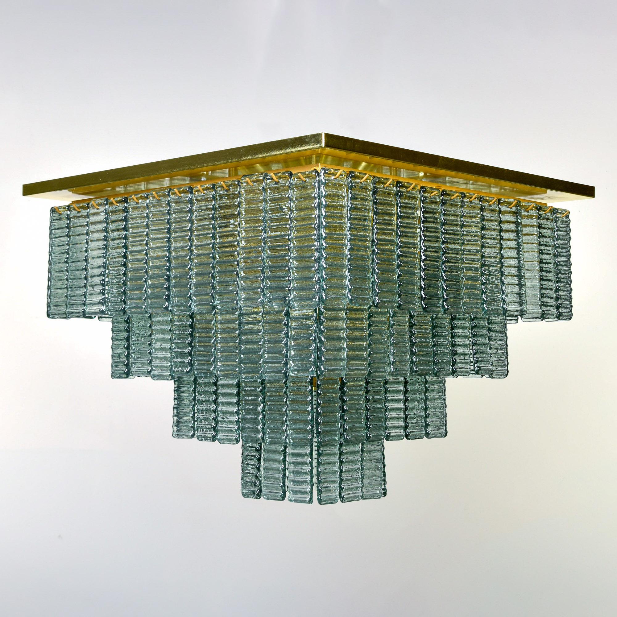 New and made for us in Italy, this flush mount fixture has 12 internal lights with standard sized sockets. Polished brass base with a square mounting plate and four tiers of hooks that support rectangular, ribbed bottle-green glass pendants