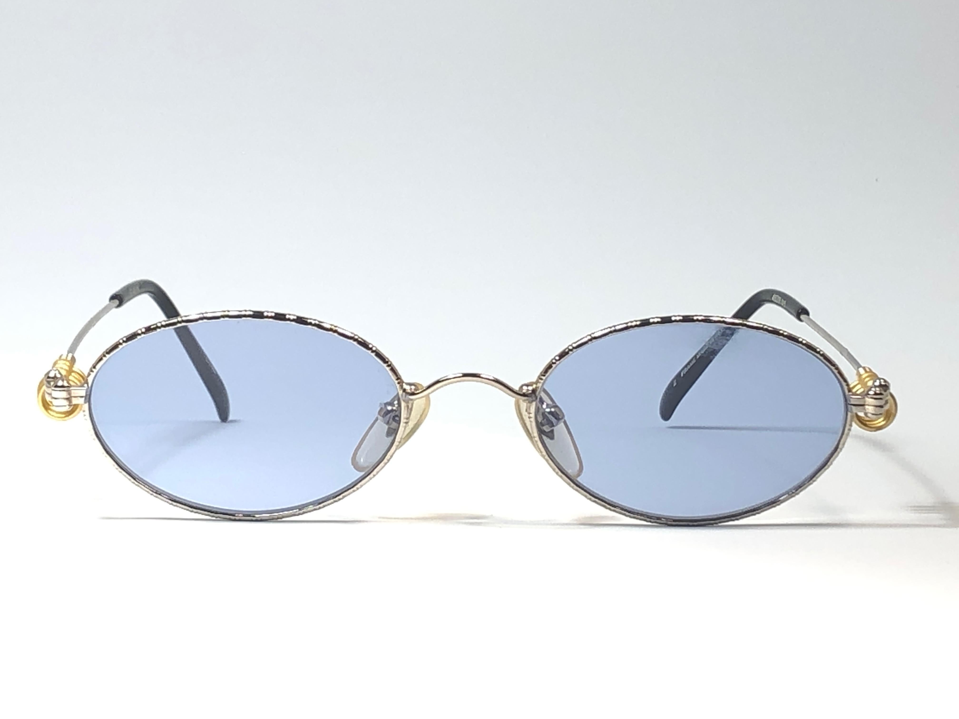 New Jean Paul Gaultier small oval silver with gold details frame. 
Spotless light blue lenses that complete a ready to wear JPG look.

Amazing design with strong yet intricate details.
Design and produced in the 1990's.
New, never worn or