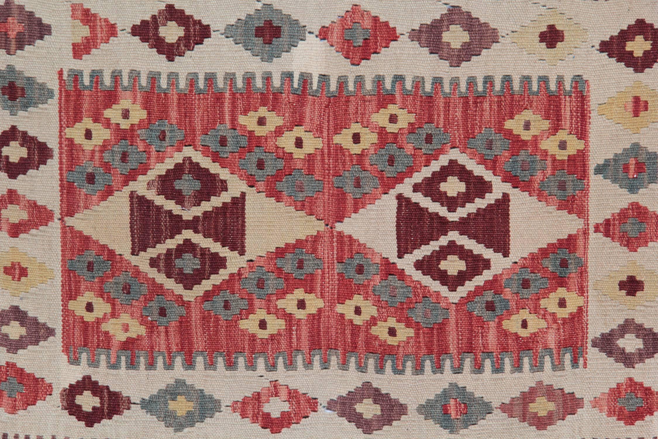 This colorful carpet rug is woven by very skilled weavers in Afghanistan, who used the highest quality wool and cotton. The flat-weave rug has orange, green, ivory, pink and red colors. The white background of this geometric rug has the same