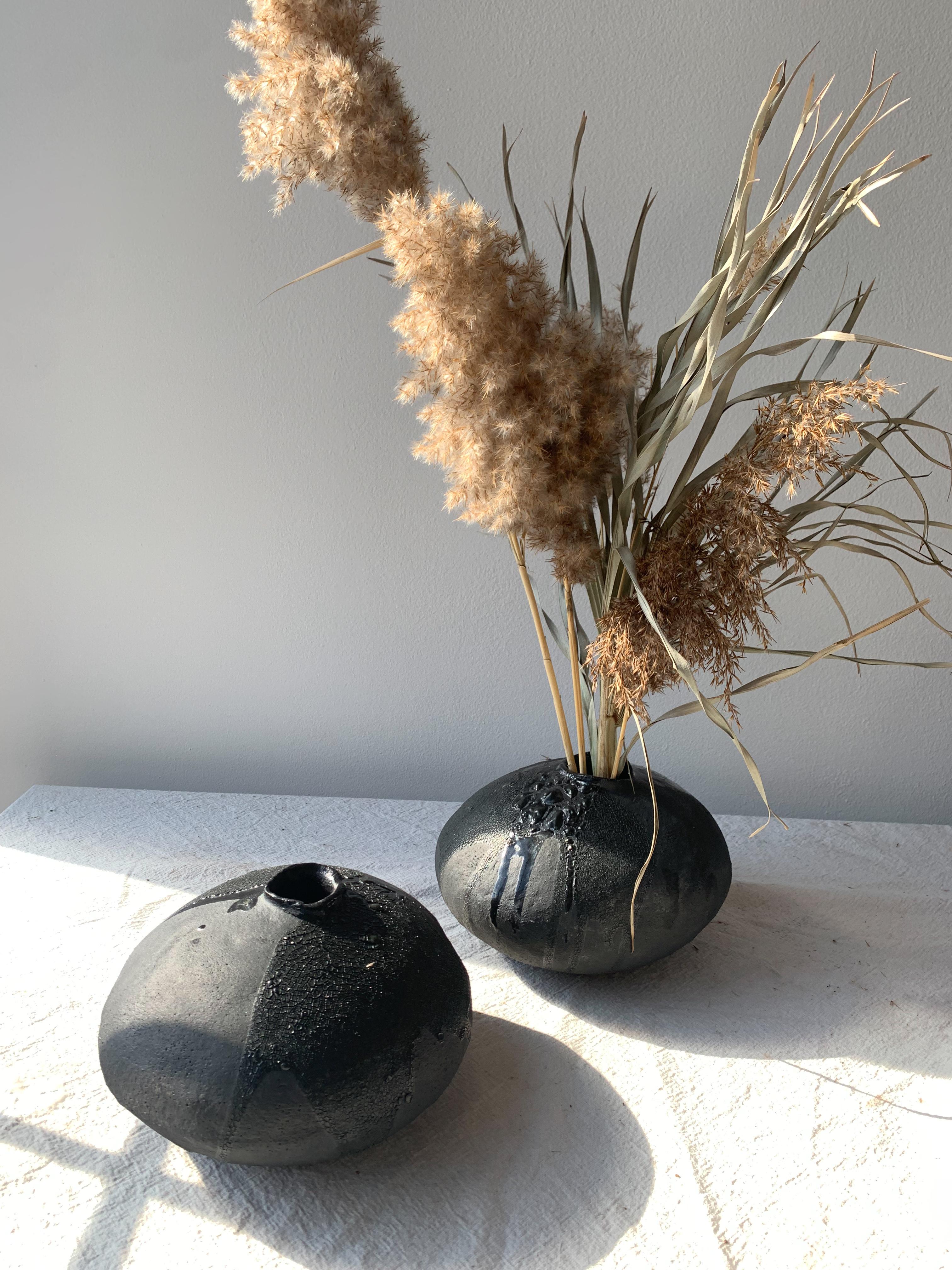 Handgefertigte, organische, moderne Vase aus einem grobkörnigen Tonkörper, der mit einer mattschwarzen Glasur überzogen ist, auf der sich Schichten von glänzender und kriechender schwarzer Glasur befinden. Jede Vase wird in unserem Atelier in