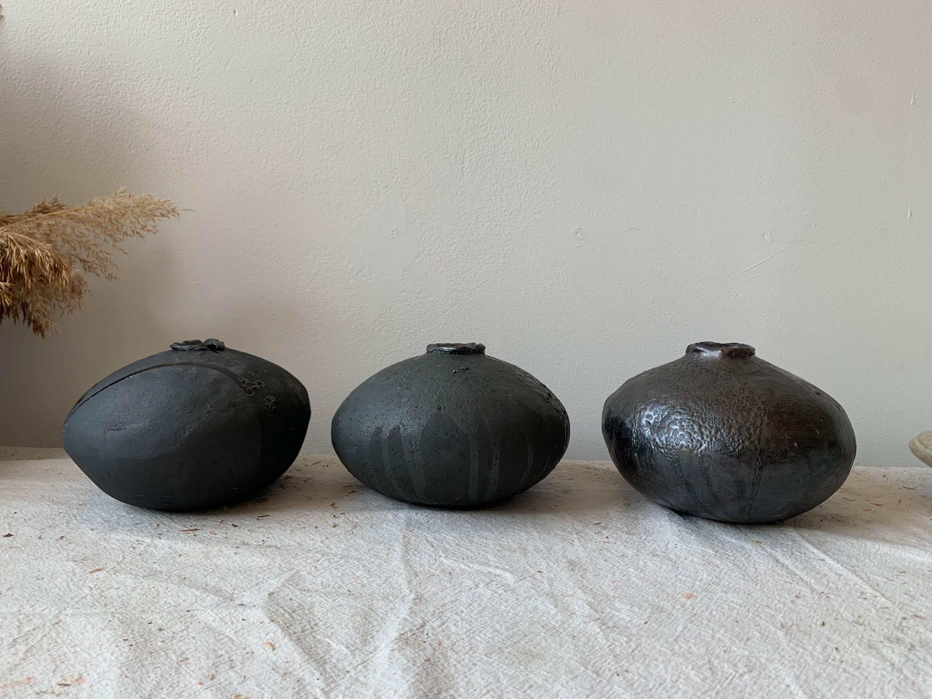 Handgefertigte, organische, moderne Vase aus einem grobkörnigen Tonkörper, der mit einer mattschwarzen Glasur überzogen ist, auf der sich Schichten von glänzender und kriechender schwarzer Glasur befinden. Jede Vase wird in unserem Studio in
