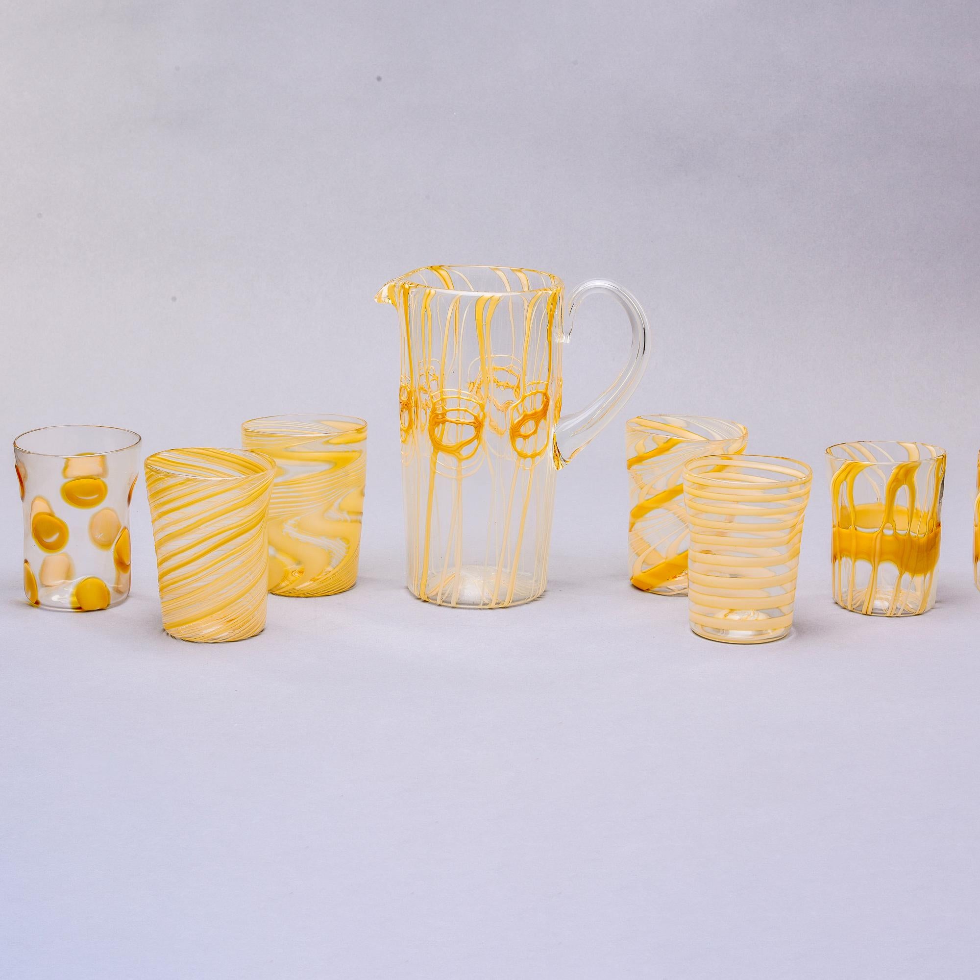 Found in Italy, this Murano glass pitcher comes with six coordinating tumblers. Pitcher is clear mouth blown glass with gold abstract decoration and tumblers has varying patterns in the same clear glass with gold decoration. Unknown Murano maker.