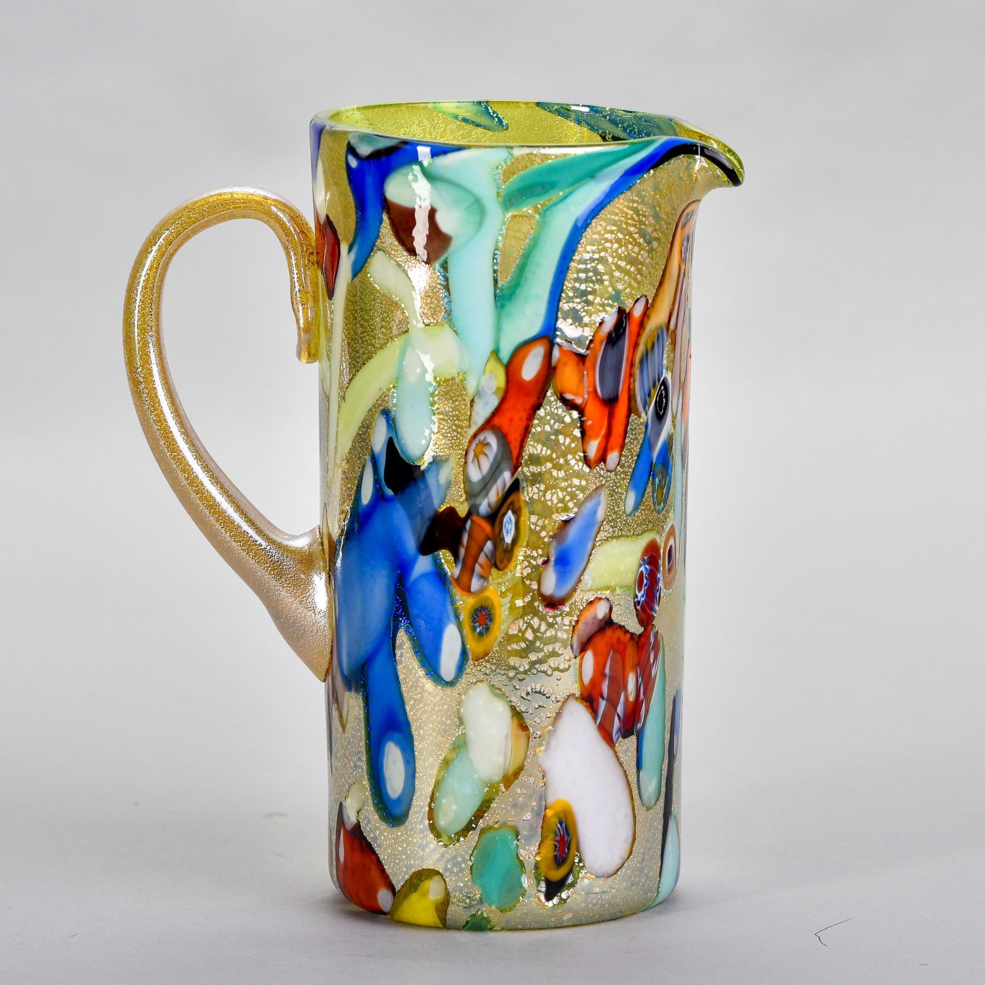 Found in Italy, this new Murano glass pitcher has an iridescent pale green gold body with multi color splatters, streaks and some scattered murrine flowers. Unknown maker. Versatile, decorative vessel than can be used as a vase or as intended.