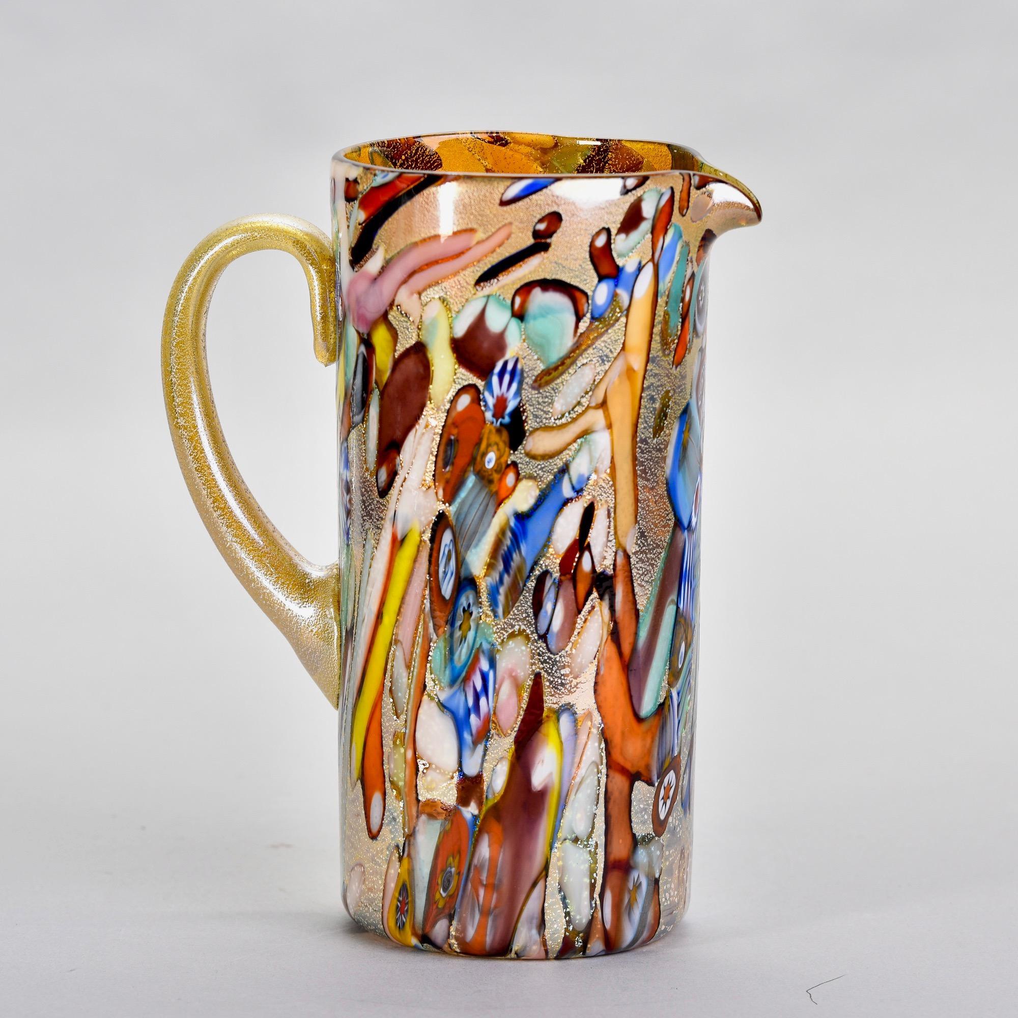 Found in Italy, this new Murano glass pitcher has an iridescent pale gold body with streaks of orange, blue white, red and some scattered murrine flowers. Unknown maker. Versatile, decorative vessel than can be used as a vase or as intended. Unknown