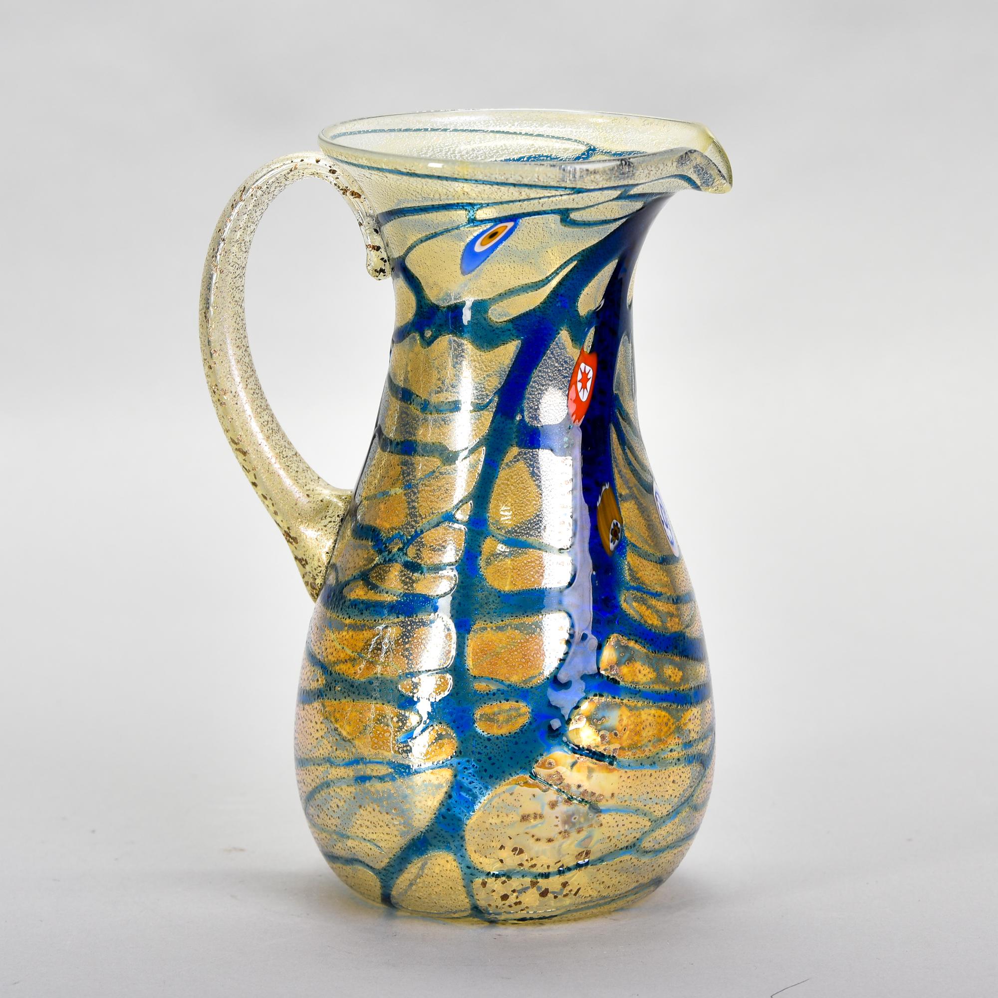Found in Italy, this new Murano glass pitcher has an iridescent pale gold body with streaks of blue and some scattered murrine flowers. Unknown maker. Versatile, decorative vessel than can be used as a vase or as intended. Unknown Murano maker.