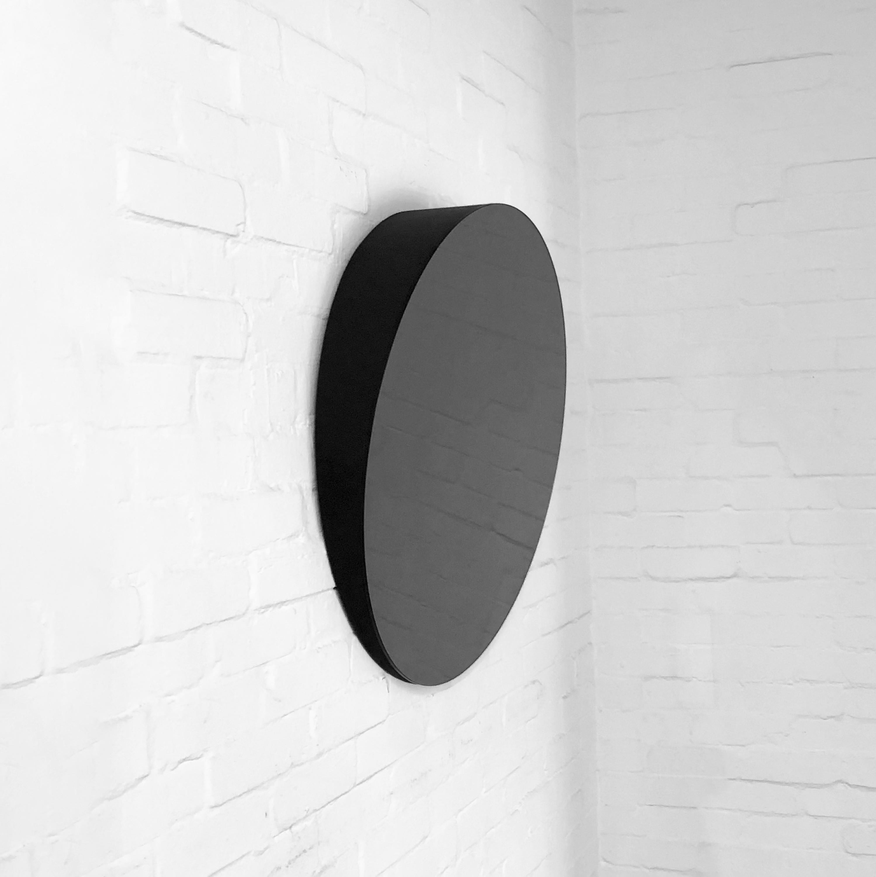 Minimalist black tinted round frameless mirror tilted 10 degrees. Designed and made in London, UK.

Fabricated with a painted MDF backing and incorporated French Cleat System (split batten) so that the mirror may hang perfectly flush with the
