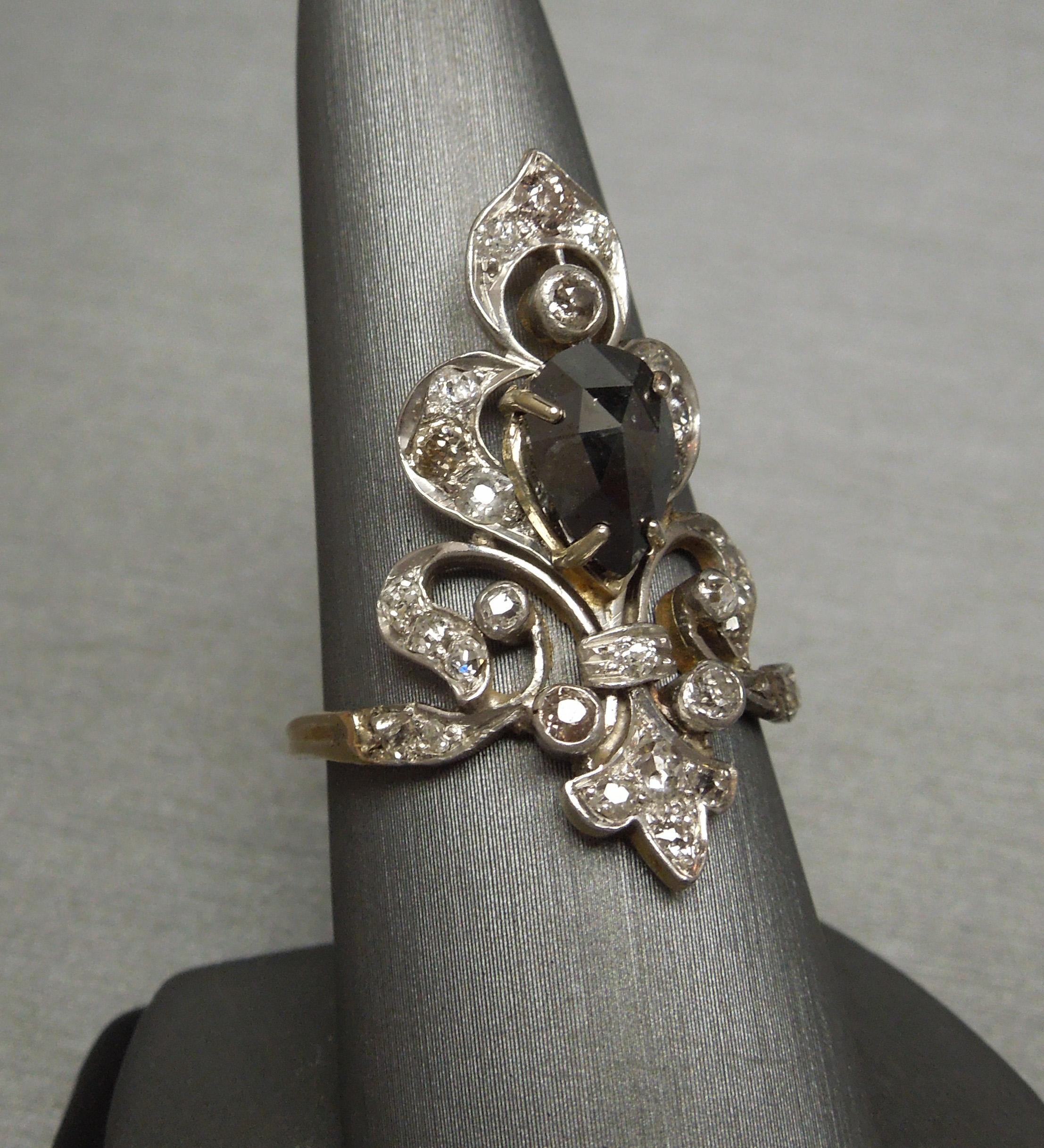 Constructed of a Sterling Silver top section & 14KT Yellow Gold base, this period Antique New Orleans Fleur de Lis Tiara style ring features a central 1.80 carat Pear cut Natural Black Diamond with several alternating White & Champagne Old European
