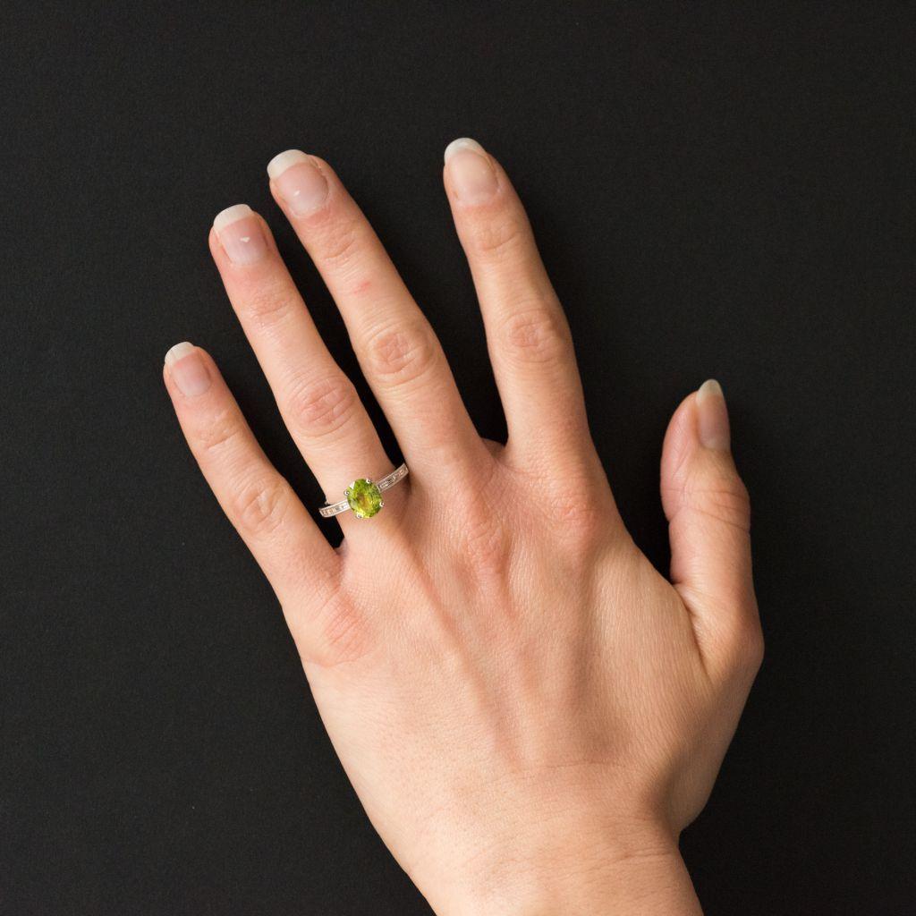 Ring in 18 karat white gold. 
This splendid peridot ring is claw set with an oval peridot. On each side the beginning of the ring band is beaded and bezel set with 5 baguette diamonds. The side of the openwork ring bed is set with 5 brilliant cut