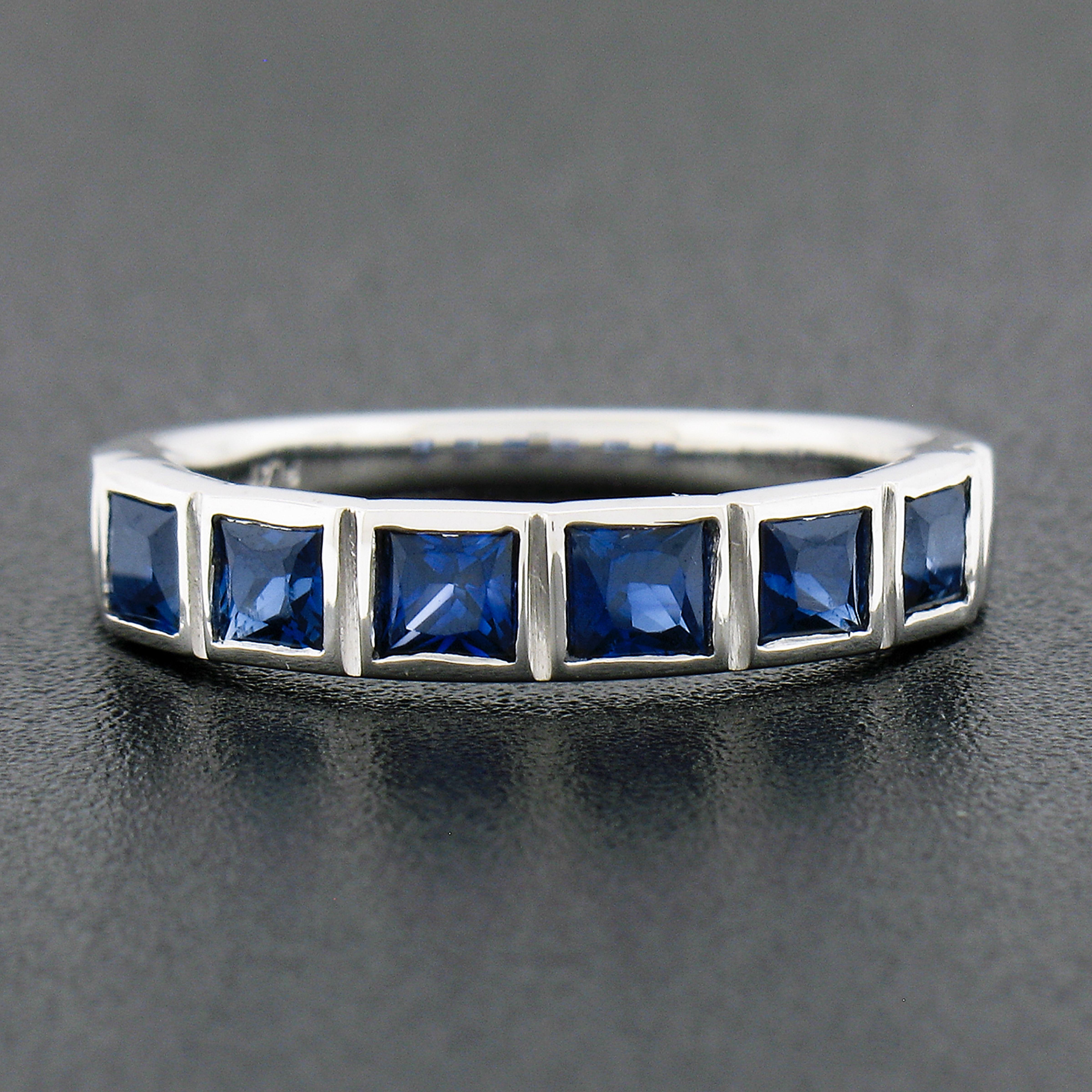 This magnificent and very well made band ring is newly crafted in solid platinum and features 6 genuine sapphire stones neatly and individually bezel set across the top. These fine sapphires are square step cut, totaling exactly 1.18 carats in