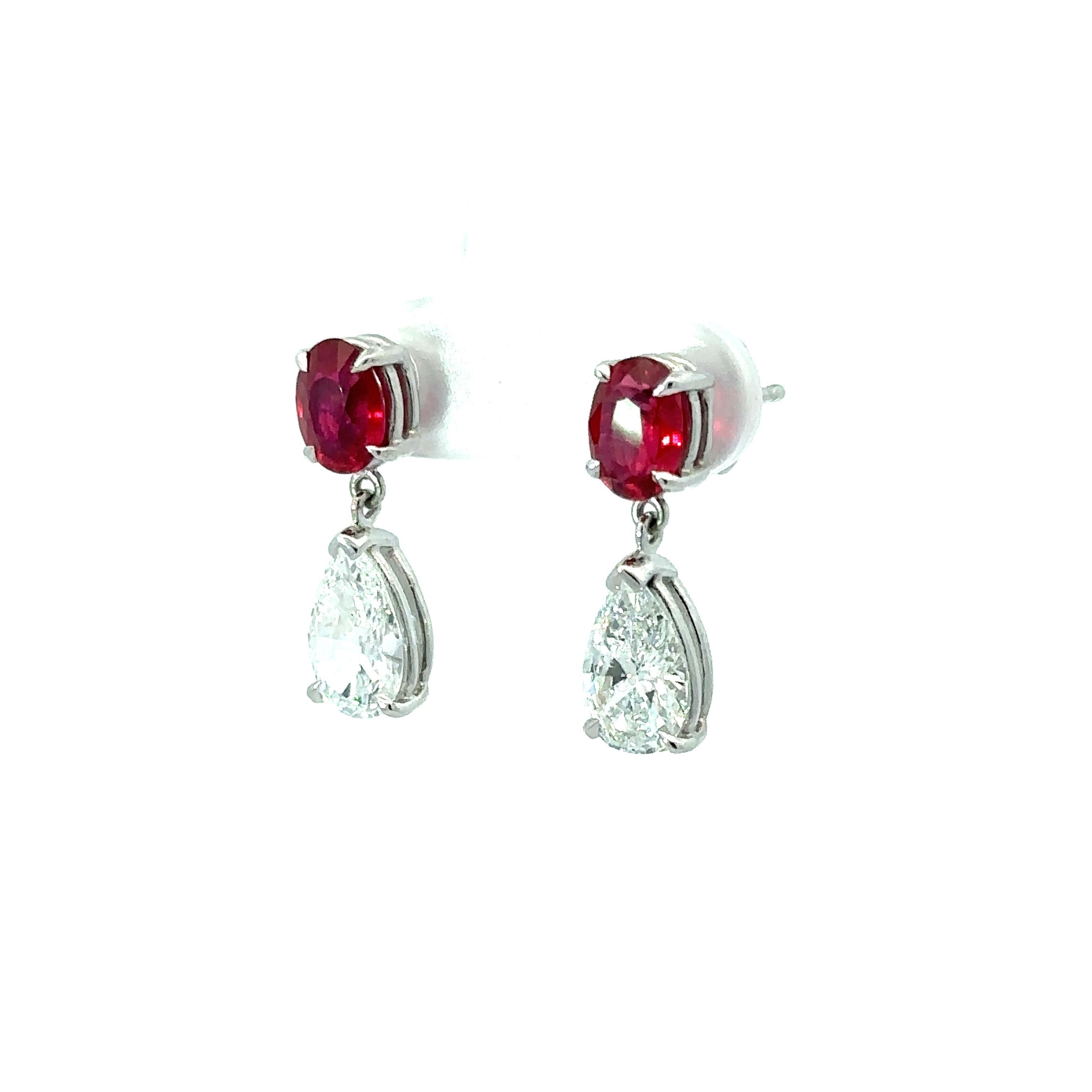 These super elegant and fancy pair of earrings is crafted in solid platinum and feature a matching pair of GIA certified oval brilliant cut rubies and pear brilliant diamonds. The rubies display very fine vivid and rich red color while the large,