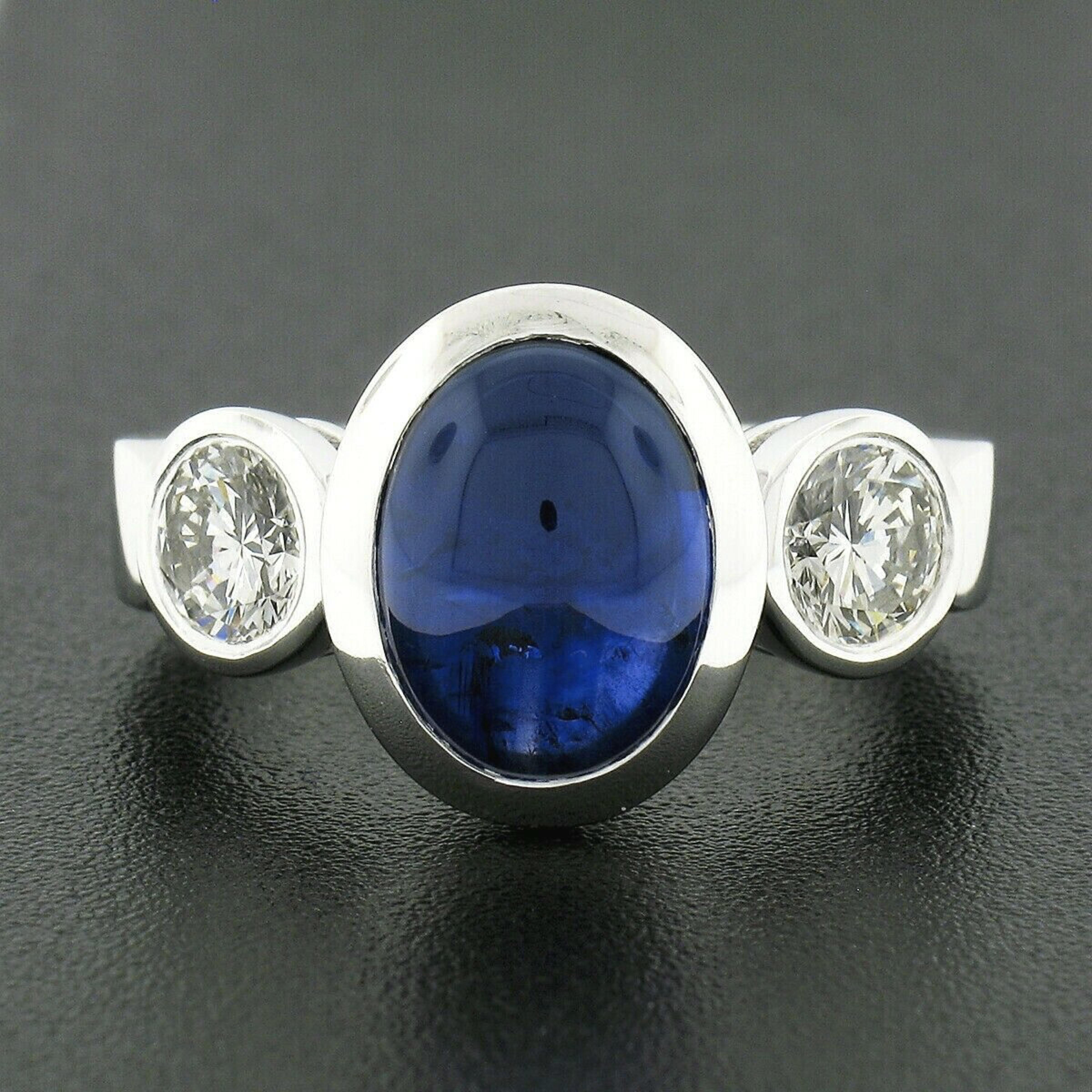 This gorgeous and very well made three-stone ring is newly crafted in solid platinum and features a magnificent, Gubelin certified, natural sapphire stone perfectly bezel set at its center. The oval cabochon cut sapphire is certified as weighing