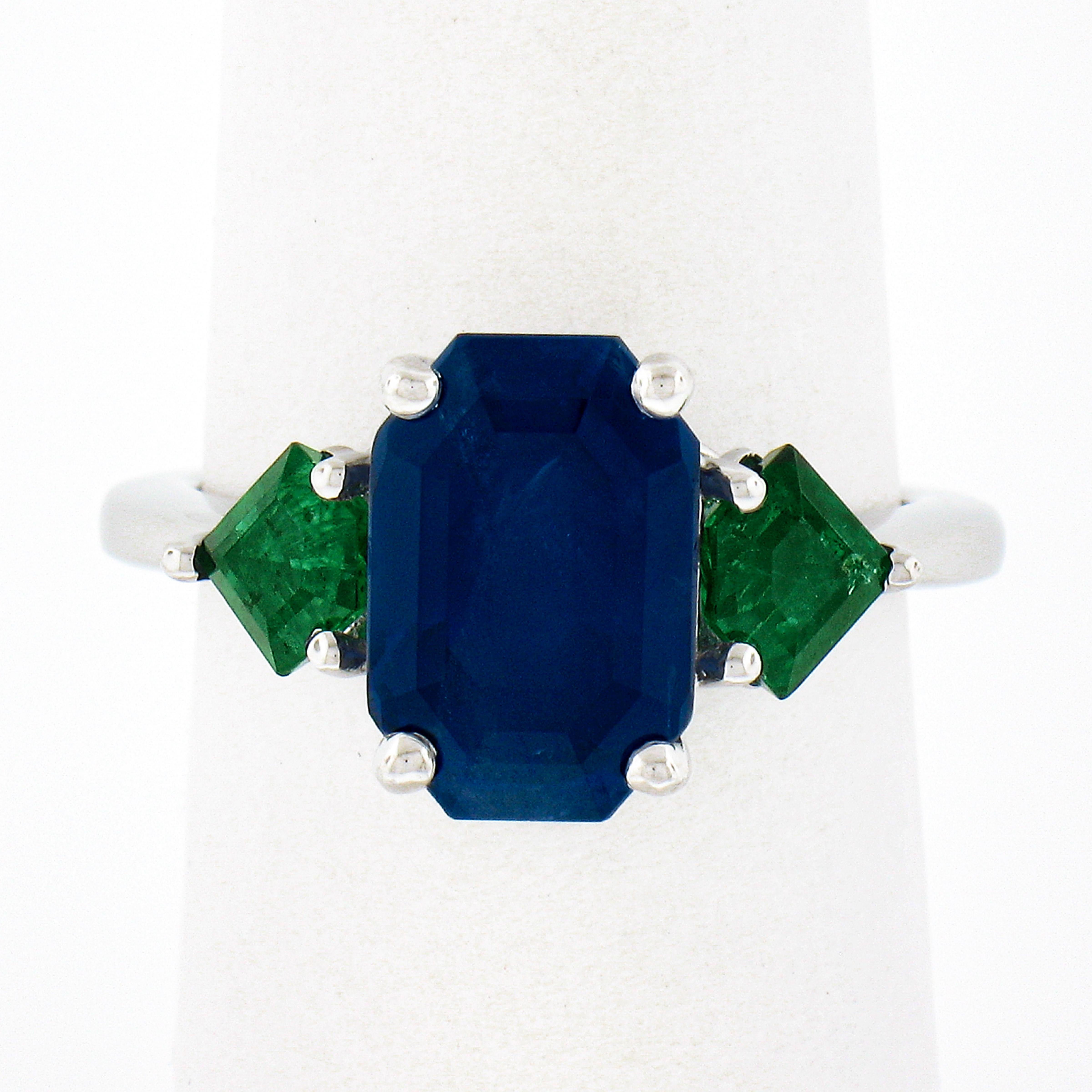 This breathtaking, custom made, sapphire and emerald engagement ring is crafted in solid platinum and features a magnificent, Gubelin certified, elongated emerald cut sapphire solitaire that's perfectly prong set at the center and flanked on either