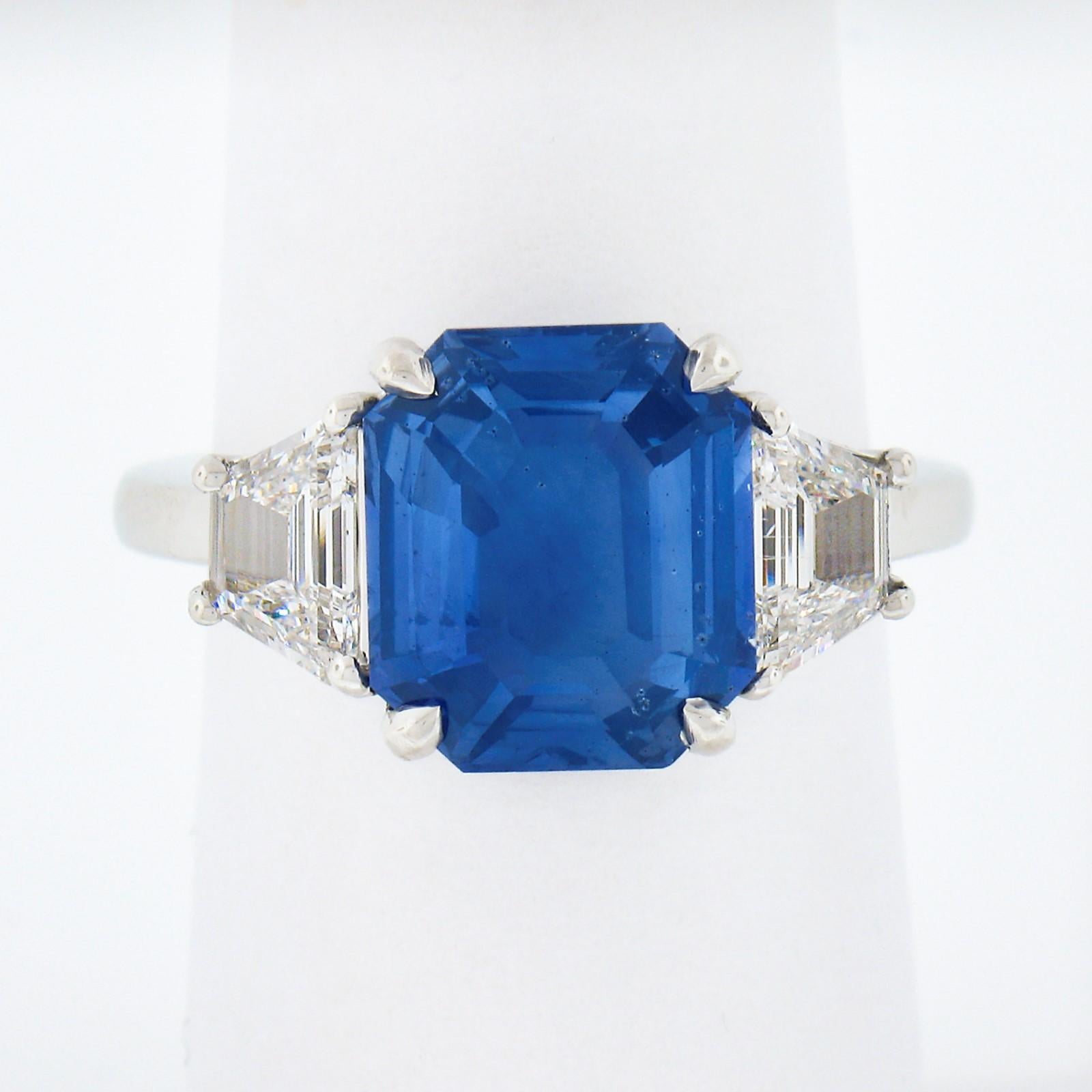 Here we have an absolutely magnificent, custom designed, sapphire and diamond three stone engagement ring that is newly crafted in solid platinum. It features a truly breathtaking, GIA certified, emerald step cut sapphire solitaire that is neatly