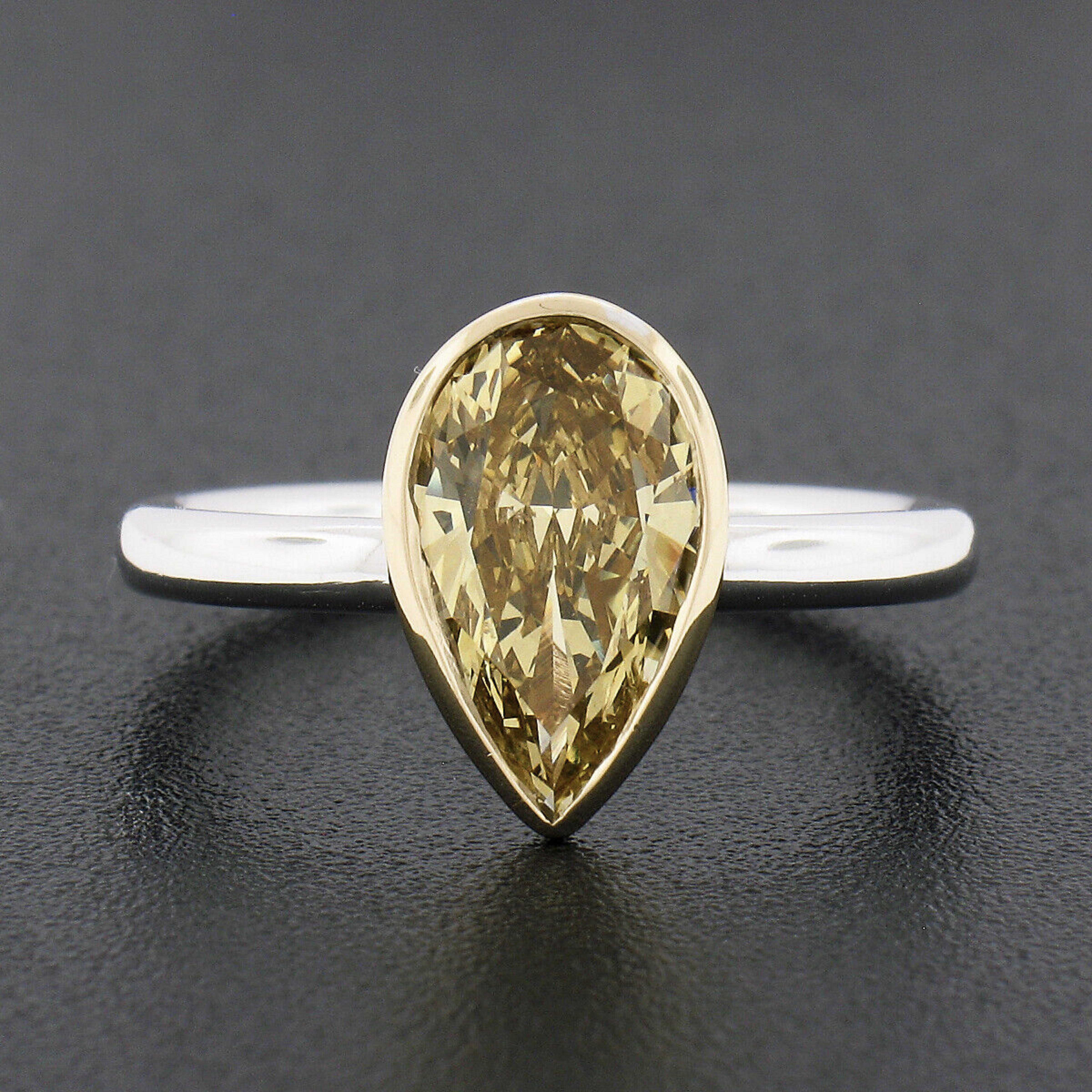 This absolutely magnificent and well made diamond solitaire engagement ring is newly crafted from solid .950 platinum with an 18k yellow gold bezel setting that features a gorgeous fancy yellow diamond. This GIA certified elongated pear cut stone is