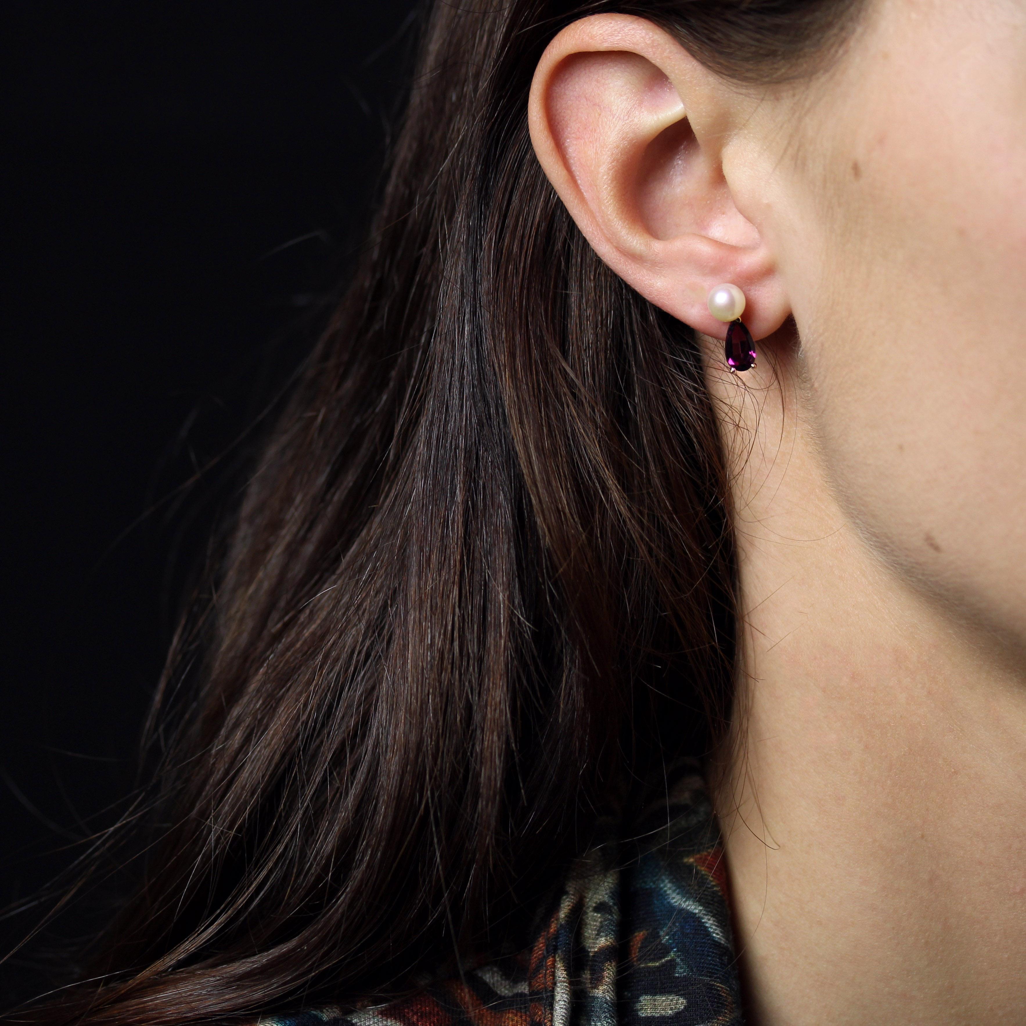 Para orejas perforadas.
Pendientes de oro amarillo de 18 quilates. 
Cada luminoso pendiente lleva una perla cultivada de botón oriental de color blanco nacarado sujeta con un cierre de botón y mariposa. Un granate rodolita en forma de pera está