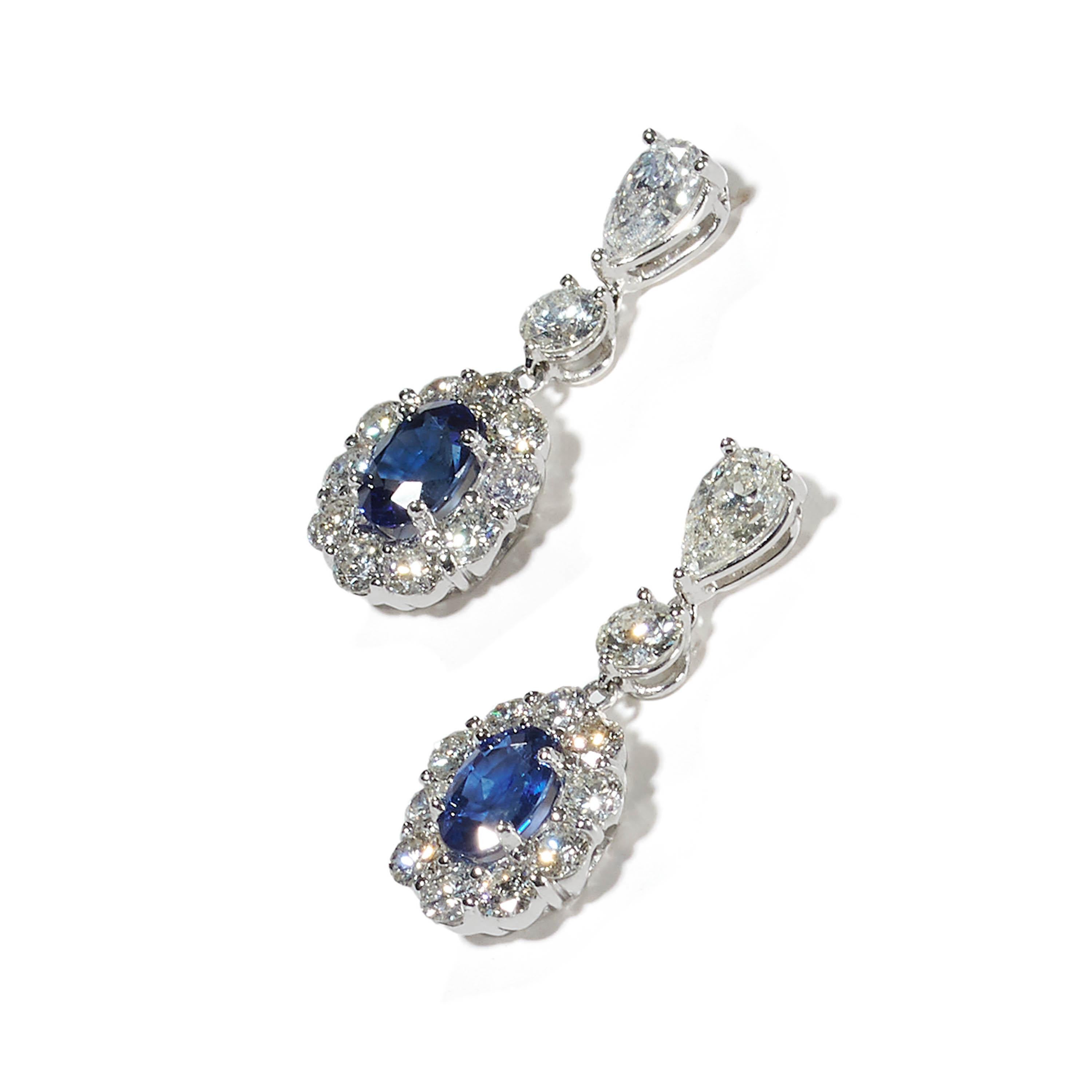 A pair of modern sapphire and diamond cluster drop earrings, each set with a pear shape diamond in the top, suspending a round brilliant-cut diamond, connecting a cluster of round brilliant-cut diamonds, with an oval faceted sapphire, in the centre,
