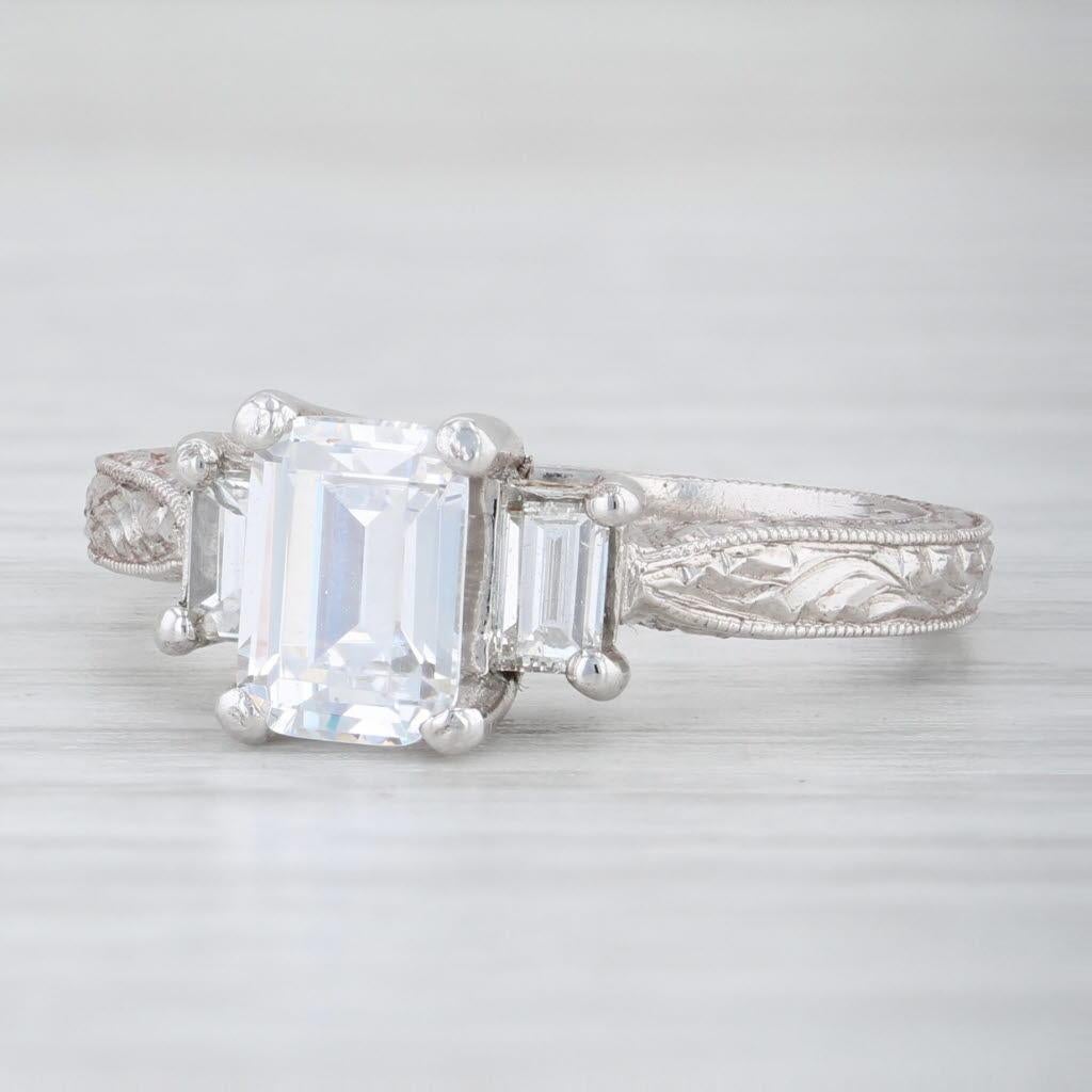 This beautiful NEW Tacori engagement ring is a semi mount 3-stone design currently set with a 1 carat emerald cut cubic zirconia, accented by genuine emerald cut diamonds to either side. The elegant band is accented by detailed floral or vinework