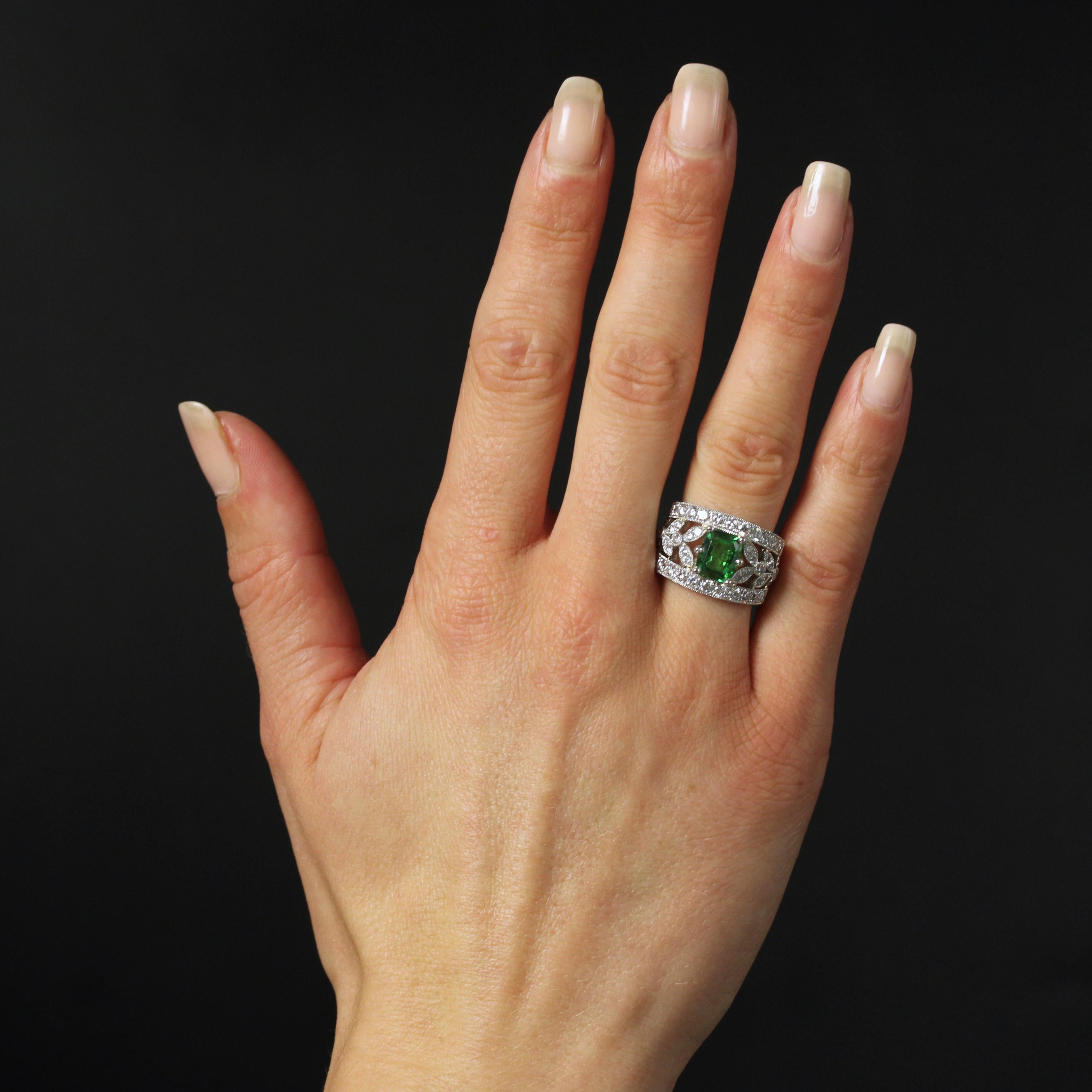 Platinum ring, dog's head hallmark.
This magnificent platinum band ring is wide and openworked with plant motifs, set with modern brilliant-cut diamonds. In the center, a tsavorite garnet and claw setting. On either side, half the rings are set with