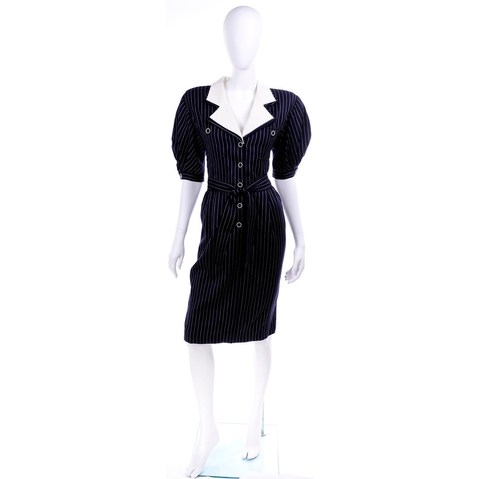 This is a vintage 1980's Dress designed by Emanuel Ungaro in a navy blue and white pinstripe with a waffle weave white collar. The dress buttons up the front and has a sash belt ,gathered, puff short sleeves and shoulder pads. It has its original