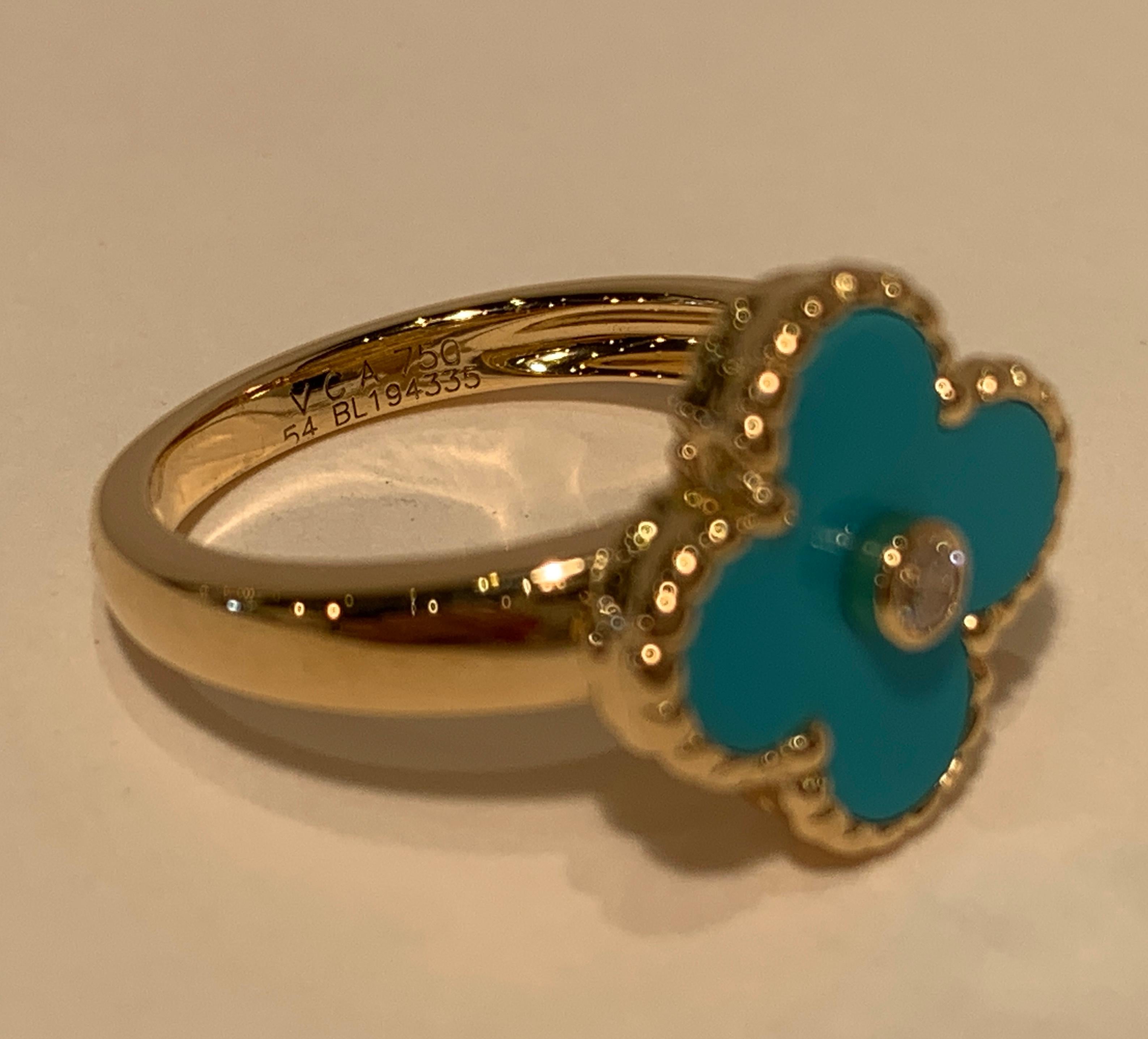 Exquisite authentic Van Cleef & Arpels 18 karat yellow gold ring of unparalleled artistry features a bright blue turquoise 4 leaf clover shaped face with a bezel set round brilliant diamond center stone. The turquoise is bezel set with beaded trim