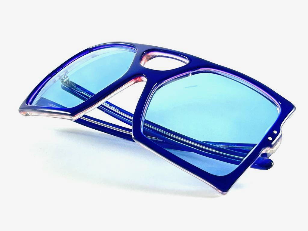 Highly collectable sunglasses signed by English Anglo American Optical.

Extra large frame with. medium blue lenses.  
New, never worn or displayed. 
This pair could show minor sign of wear due to storage. Made in England.

FRONT 14.5 CMS
LENS