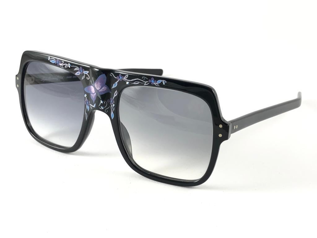 Highly collectable sunglasses signed by English Anglo American Optical.

Black frame with handprinted butterfly and leafs accents. Gradient grey lenses.  
New, never worn or displayed. 
This pair could show minor sign of wear due to storage. Made in