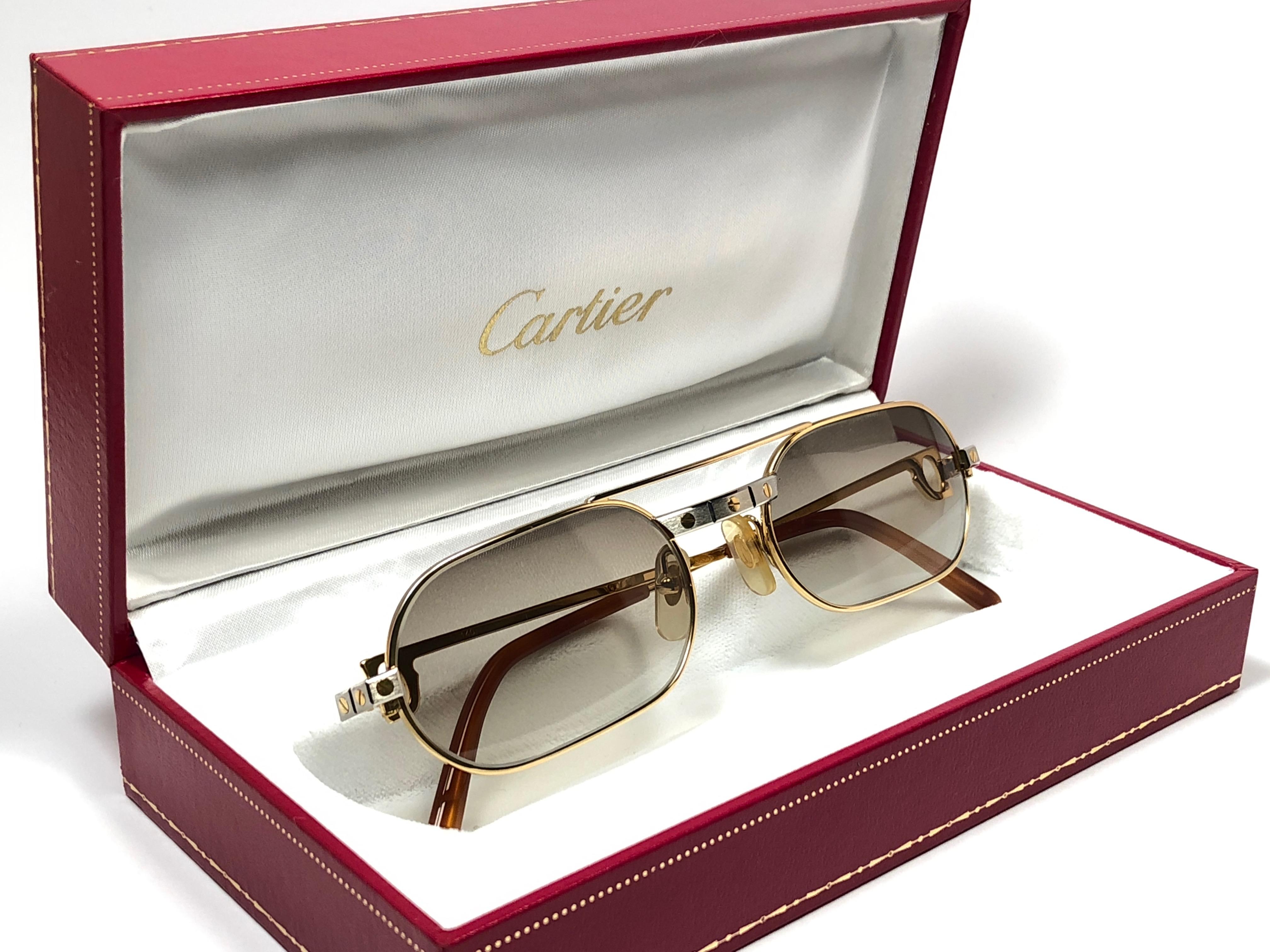 Original Cartier Santos Must Sonnenbrille von 1983 mit neuen braun verlaufenden Gläsern. Der Rahmen ist mit der Vorderseite und den Seiten in Gelb- und Weißgold und den berühmten Santos-Akzenten.  
Alle Markenzeichen. rote Emaille mit