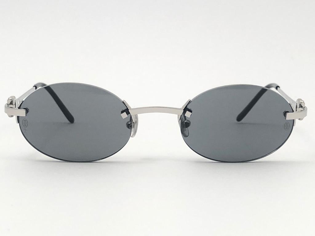 New 1990 Cartier Shamal unique rimless sunglasses with grey (uv protection) lenses. Frame with the front and sides in platine. All hallmarks. 

Cartier gold signs on the black ear paddles. 

Please notice this item its nearly 30 years old and may