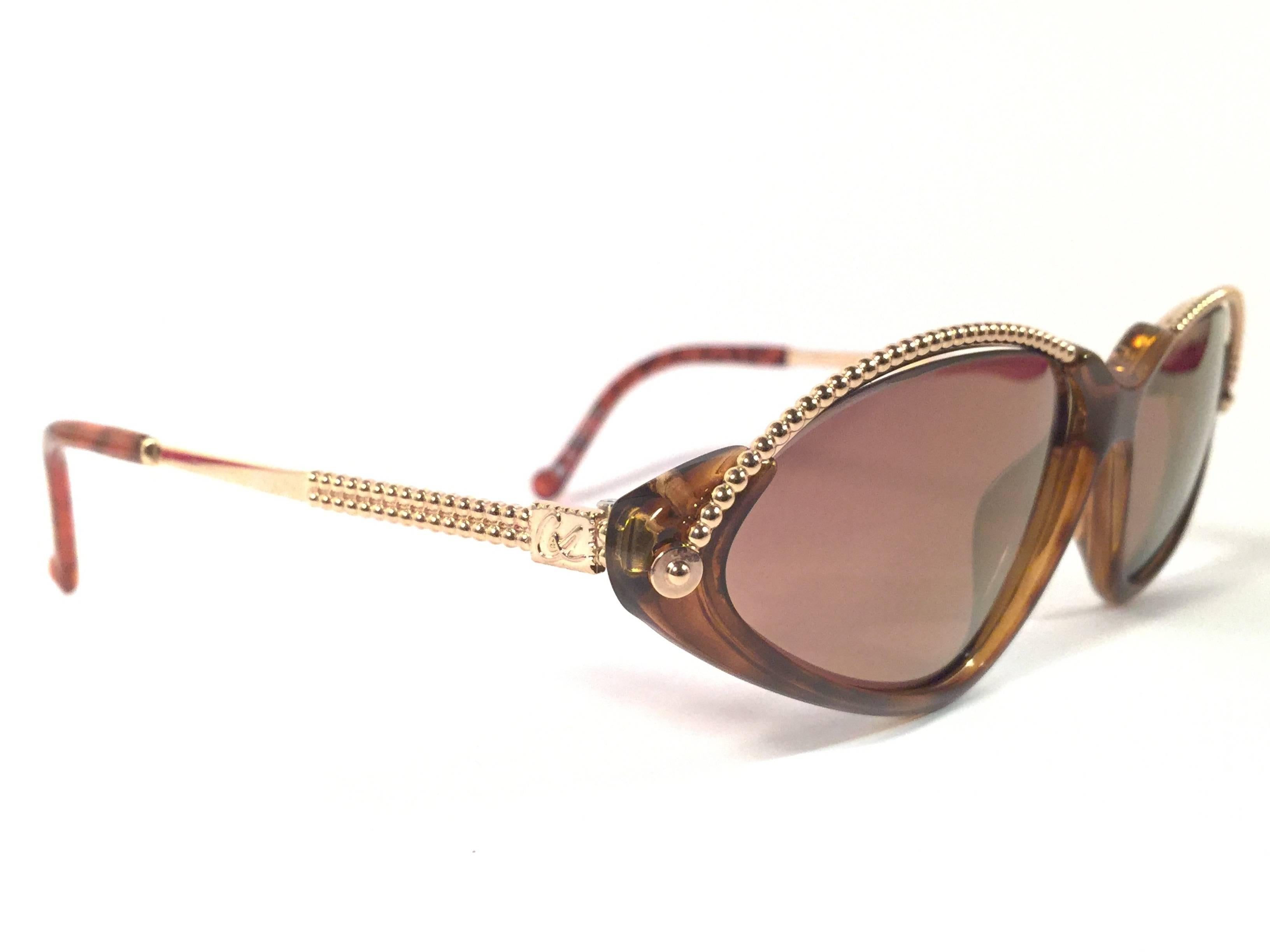 Rare pair of New vintage Christian Lacroix sunglasses. 

Tortoise with elaborated gold accents, cat eyed shaped frame holding a pair of spotless dark amber lenses.

New, never worn or displayed. Made in France.

FRONT : 14 CMS

LENS HEIGHT : 3.5
