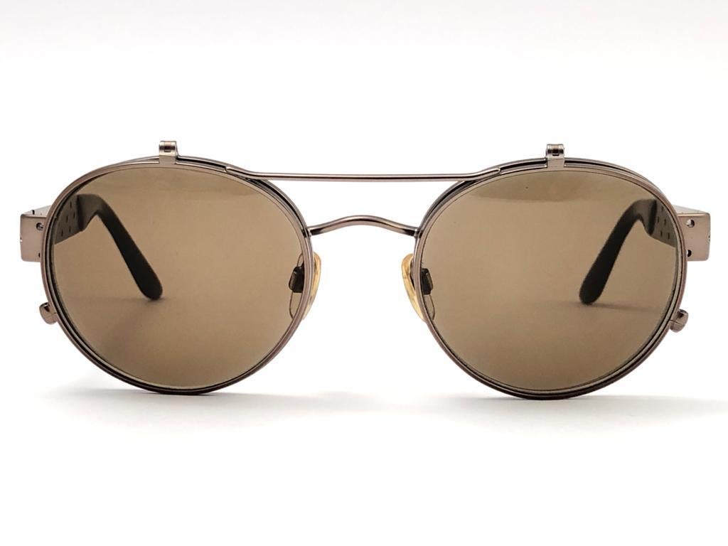 New Vintage Giorgio Armani round featuring a flip top system. Grey medium lenses.

Made in Italy.
 
Produced and design in 1990's.

New, never worn or displayed.

FRONT : 13.5 cms
LENS HEIGHT : 4.7 CMS
LENS WIDTH : 5 CMS
TEMPLES : 12 CMS
