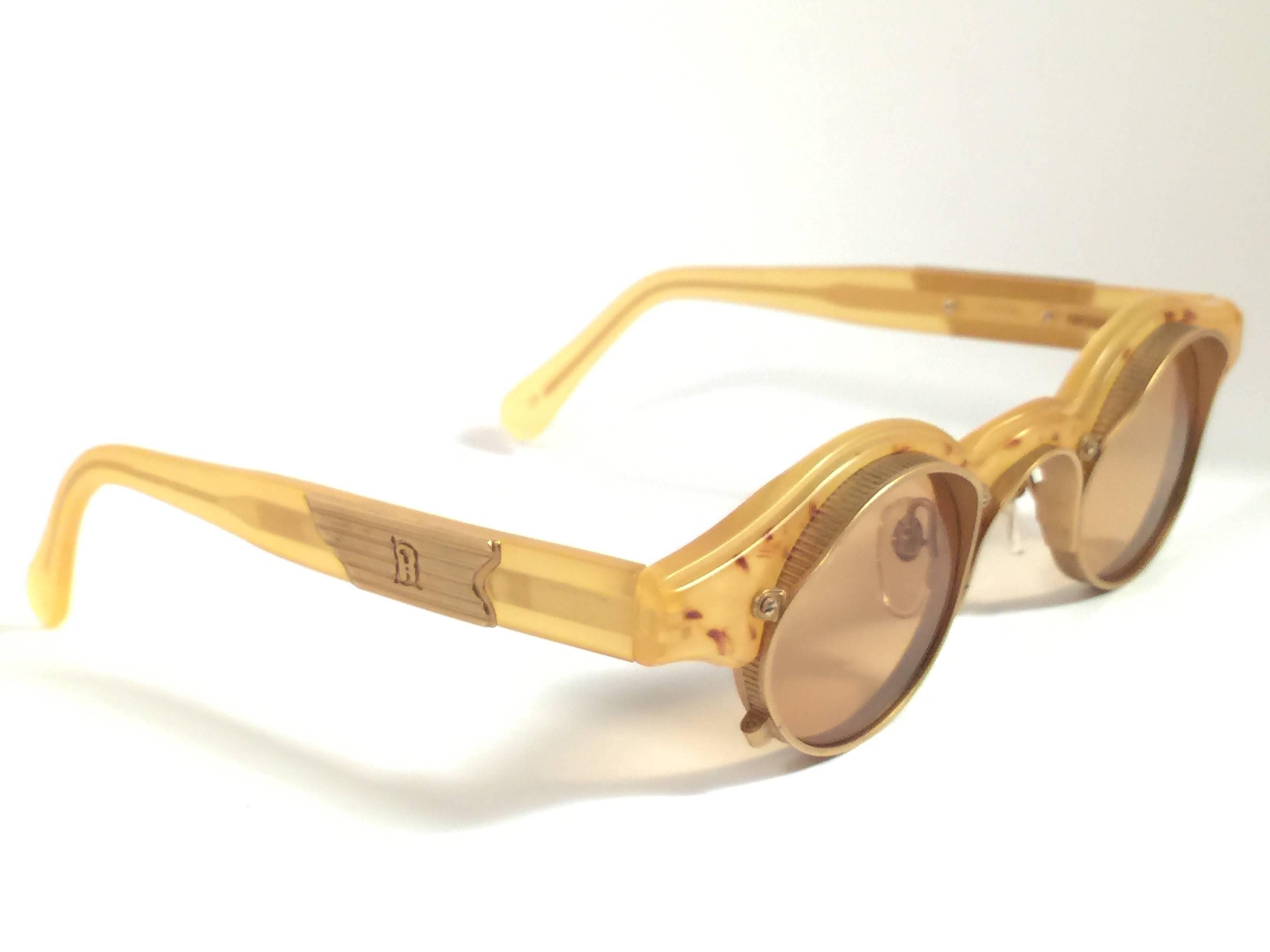 New vintage made in japan Matsuda Sonnenbrille. Runder klarer gelber Rahmen mit goldenen Einsätzen, der ein makelloses Paar bernsteinfarbener Gläser hält.
 
Neu, nie getragen oder ausgestellt. 
 
Auf dem rechten Innenbügel steht 