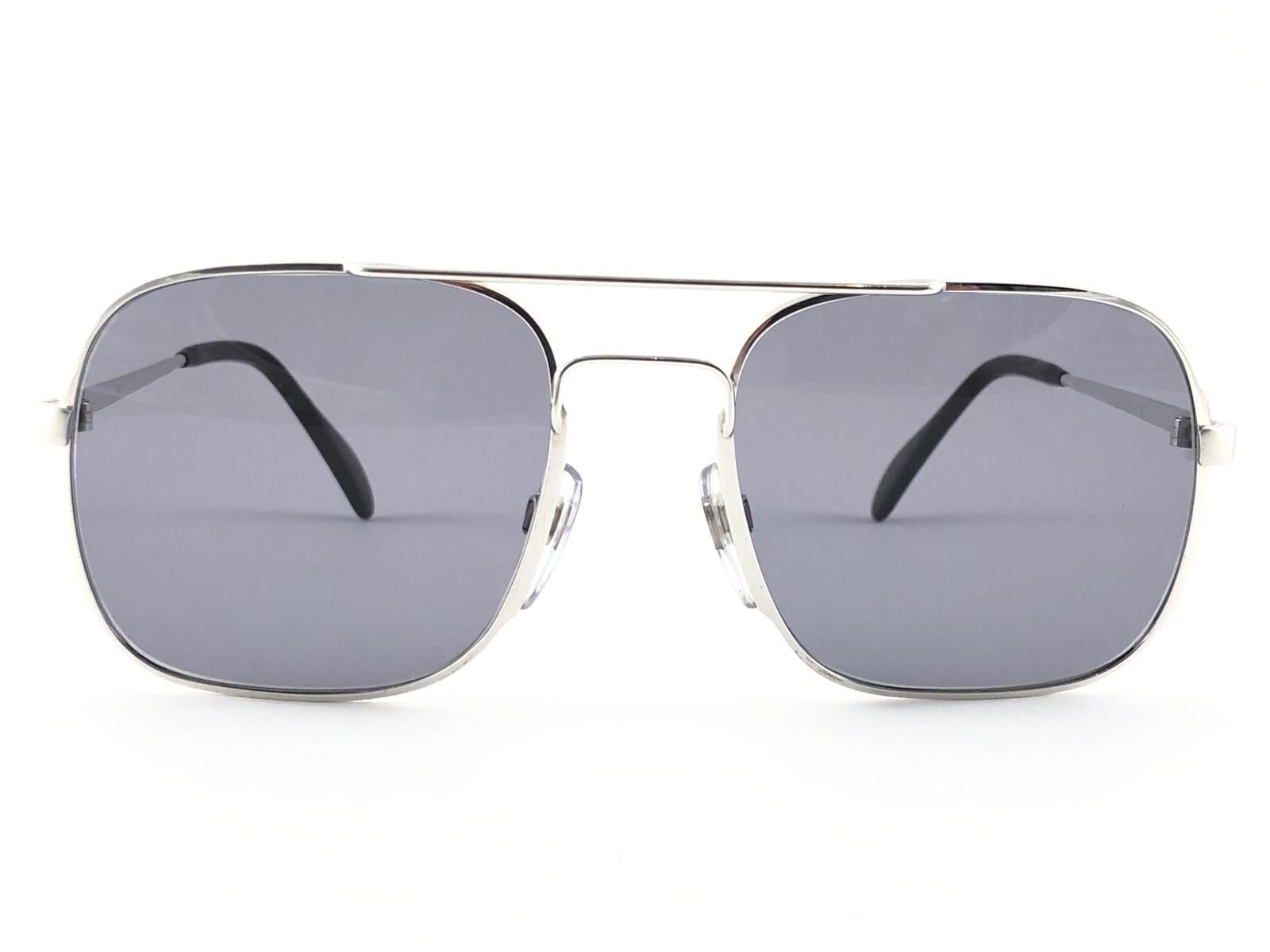 New Vintage Collector Item Menrad M367 Silver Aviator frame Sunglasses holding a pair of medium grey lenses.  

Hergestellt in Deutschland in den 1970er Jahren.



Vorderseite :                    14 cm 

Höhe der Linse :        5,1 cm