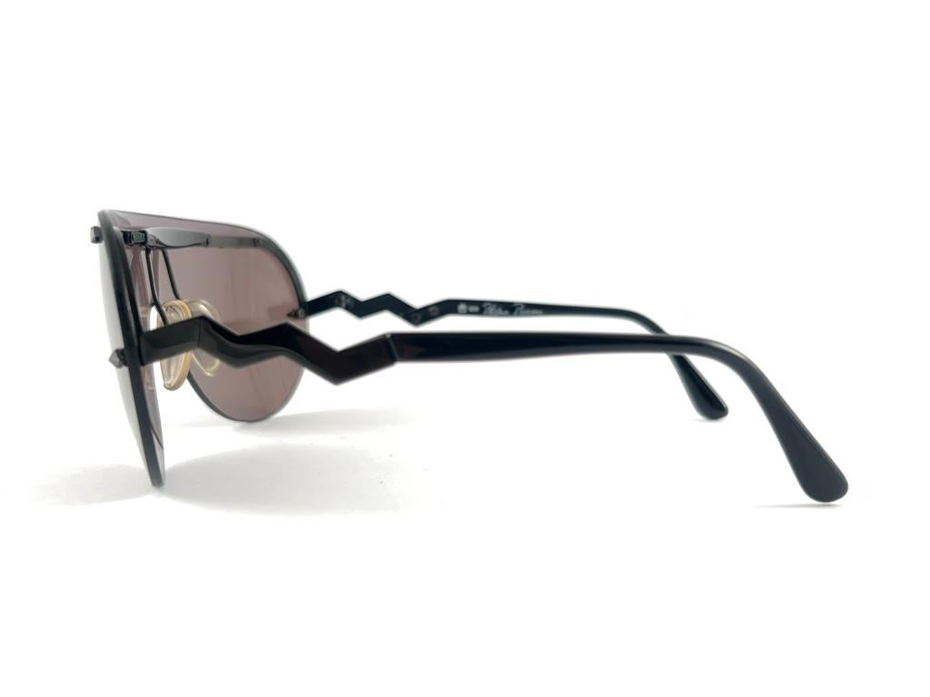 New Vintage Paloma Picasso Sunglasses Made In Germany 1980's.   

Une monture en forme de bouclier noir contenant un magnifique objectif mono en gris moyen. 

Le cadre peut présenter des signes mineurs d'utilisation en raison du stockage.  