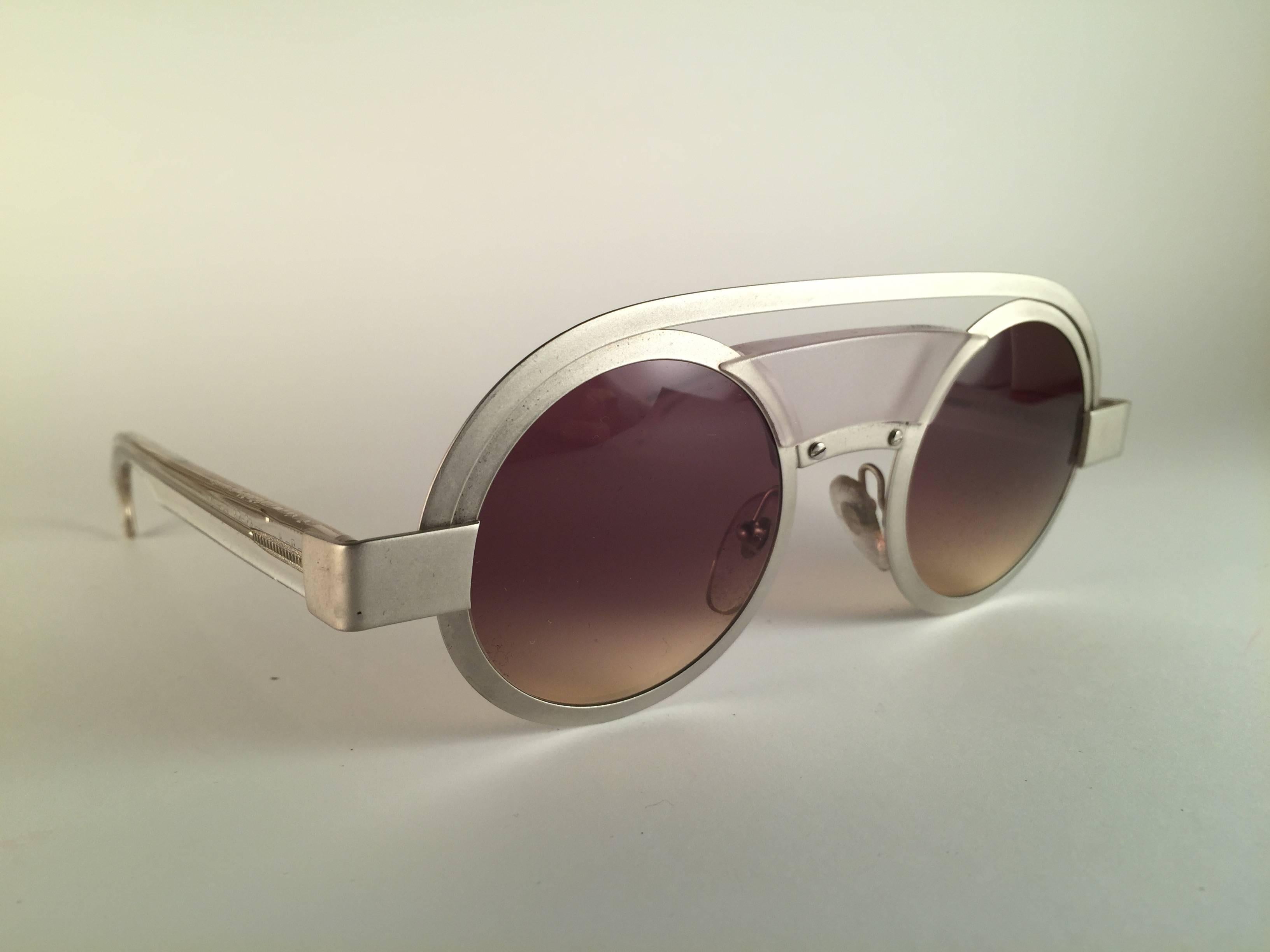 New Vintage Rare Alain Mikli Round Aluminium frame.

Seltener Artikel in neuem und ungetragenem Zustand. Makellose hellbraune Verlaufsgläser.

Bitte bedenken Sie, dass dieser Artikel fast 40 Jahre alt ist und daher durch die Lagerung leichte