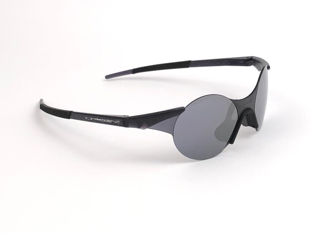 New Vintage are Oakley Sunglasses. Wrap black & grey sports frame with grey mirror lenses.
New never worn or displayed. This item might show minor sign of wear due to storage.

Made in Germany.

FRONT 14
LENS HEIGHT 4.8
LENS WIDTH 4.8
TEMPLES 13