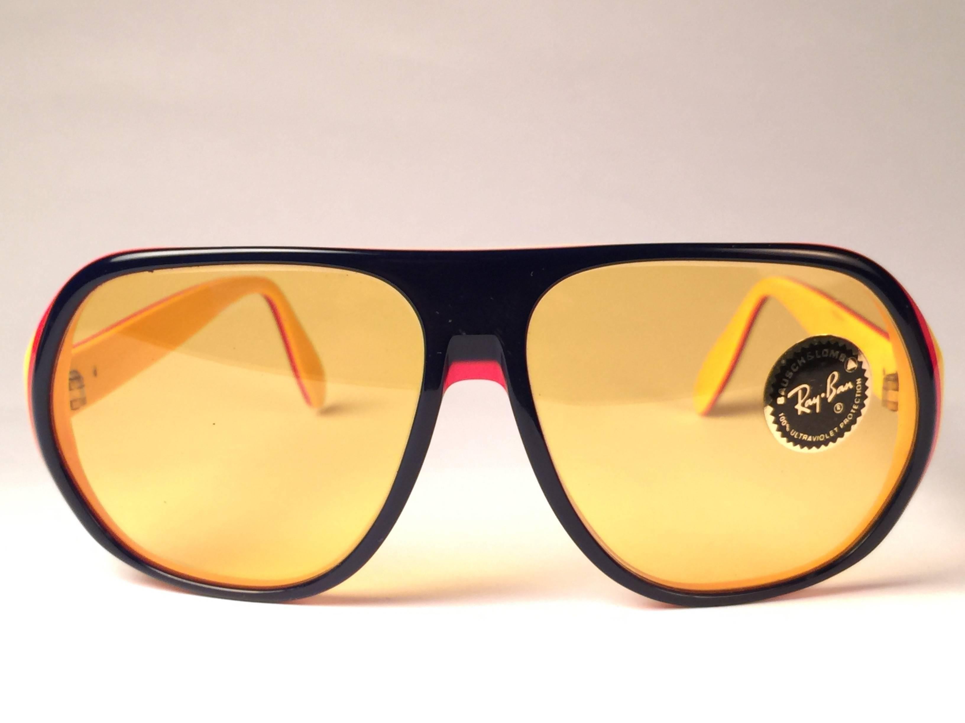 Nueva y rara montura Vintage Blazer azul, roja y amarilla que sujeta un par de lentes Ambermatic.  
Nueva, nunca usada ni expuesta.  Este par puede tener pequeños signos de desgaste tanto en las lentes como en la montura debido a los casi 40 años de