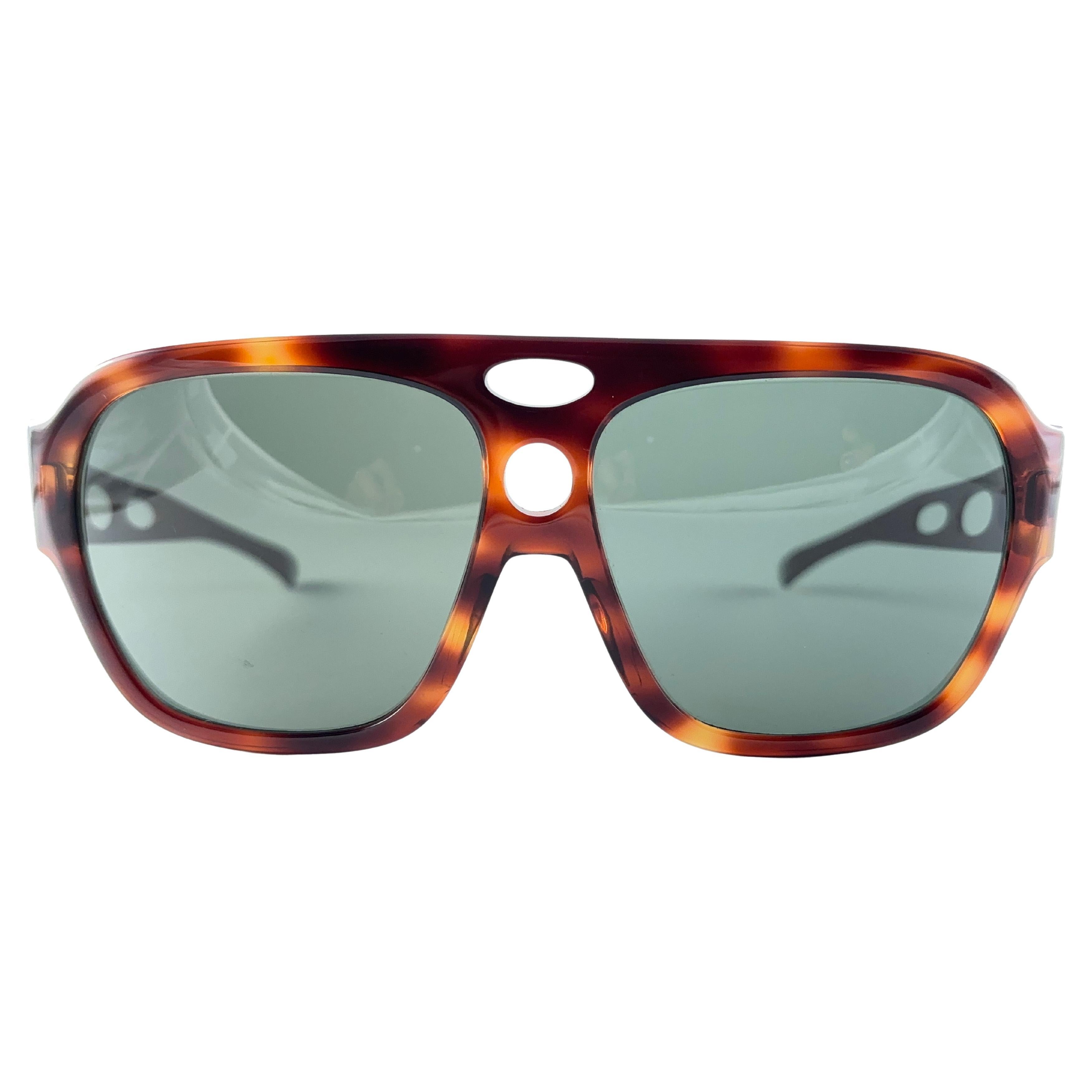 New And Rare Vintage Corrigan Ii Tortoise Frame With Perforated Metal Temples Holding A Pair Of G15 Grey Lenses.  

This Pair Have Minor Sign Of Wear Due To Nearly 40 Years Of Storage. Designed And Produced In Usa.

Front : 15 Cms 

Lens Height : 5