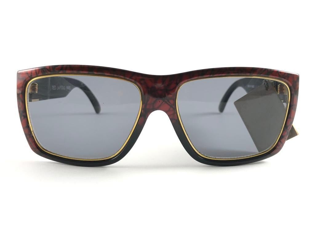 New Vintage Ted Lapidus TL 19 metallic red & gold frame with medium grey lenses.  
Made in Paris.  
Produced and design in 1970's.  
New, never worn or displayed, this item may show minor sign of wear due to storage.

MEASUREMENTS 

FRONT : 14 CMS