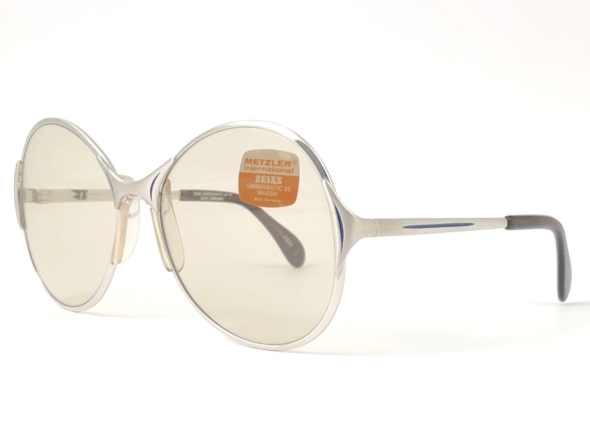Gafas de sol Zeiss Umbramatic Fabricadas en Weest Alemania Años 80. 

Montura plateada sobredimensionada que sujeta un par de lentes de color marrón medio impecables. Cuadro con pequeños desgastes debidos al almacenamiento.  

Fabricado en