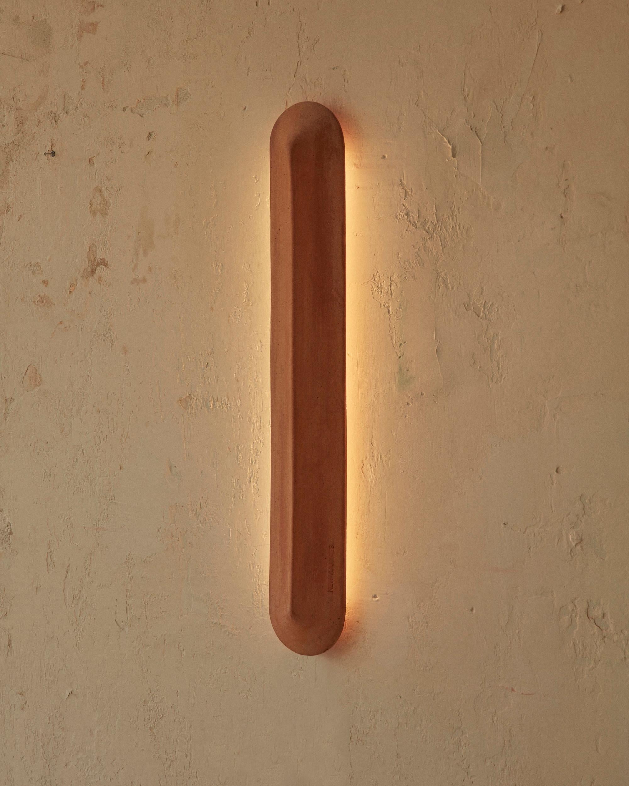 An elegant, elongated wall light, offered in two lengths – 400 millimetres and 900 millimetres. Its shield-like form is characterised by a central sharp line or ‘pinch’ that allows light to fall differently on each side of the terracotta,
