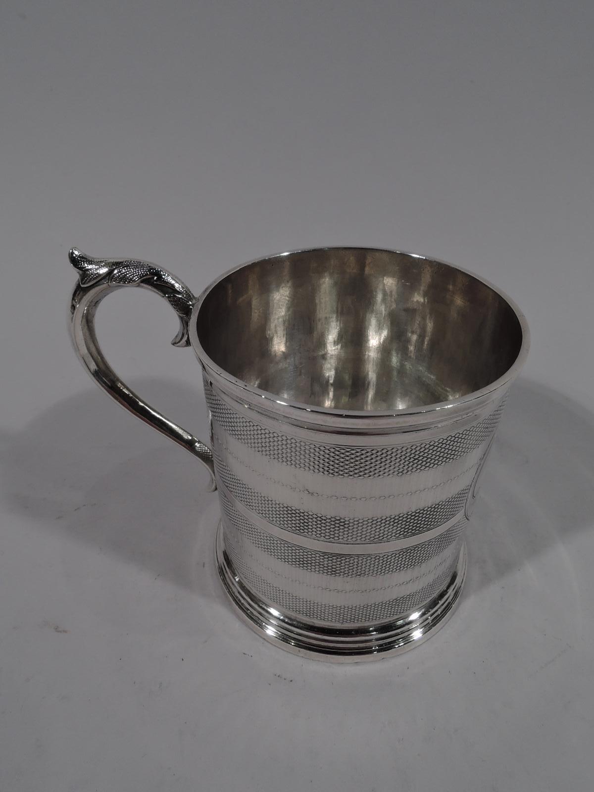 Stylish American Classical coin silver baby cup. Made by Wood & Hughes in New York, circa 1860. Straight sides with stepped and skirted foot, and leaf-capped S-scroll handle. Body has engine-turned bands and strapwork cartouche (vacant). Fully